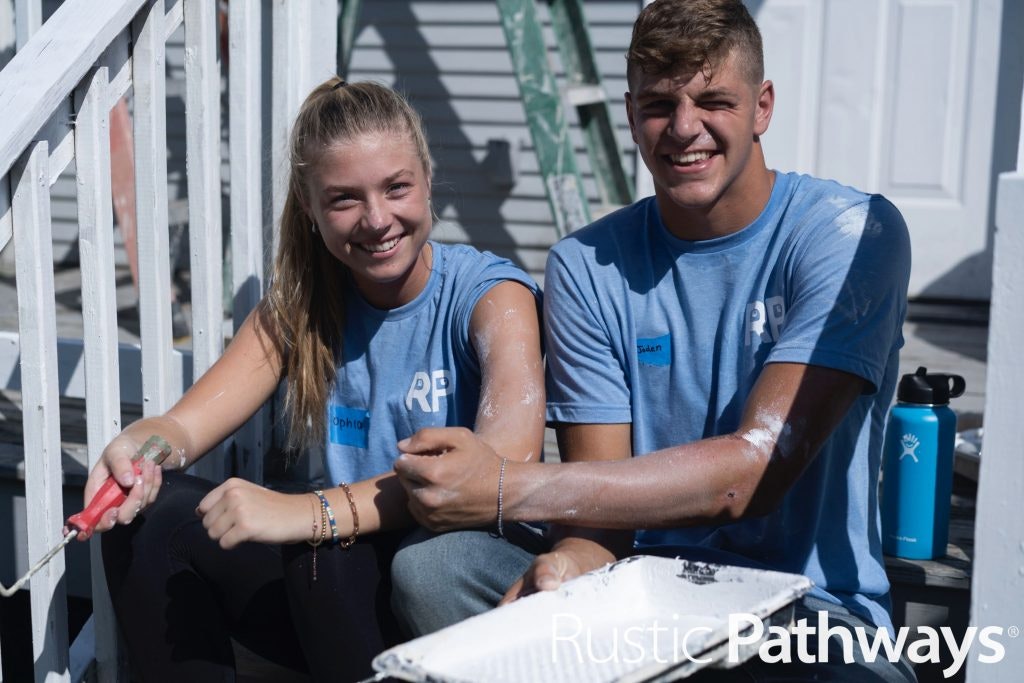 Two high school students covered in paint, smiling and taking a break during a service project in New Orleans.