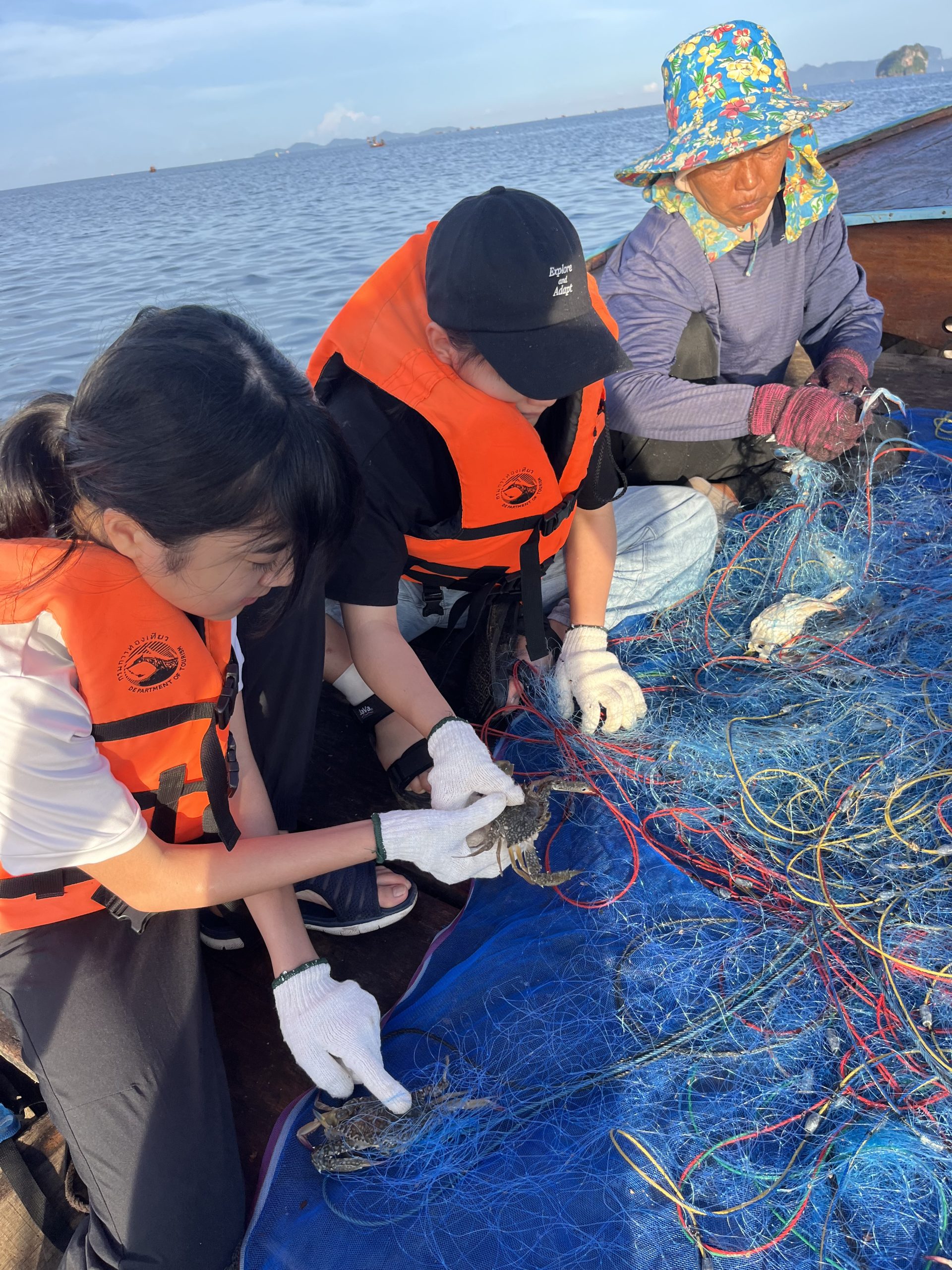 Students wearing life jackets sort fishing nets on a boat with a local fisherman