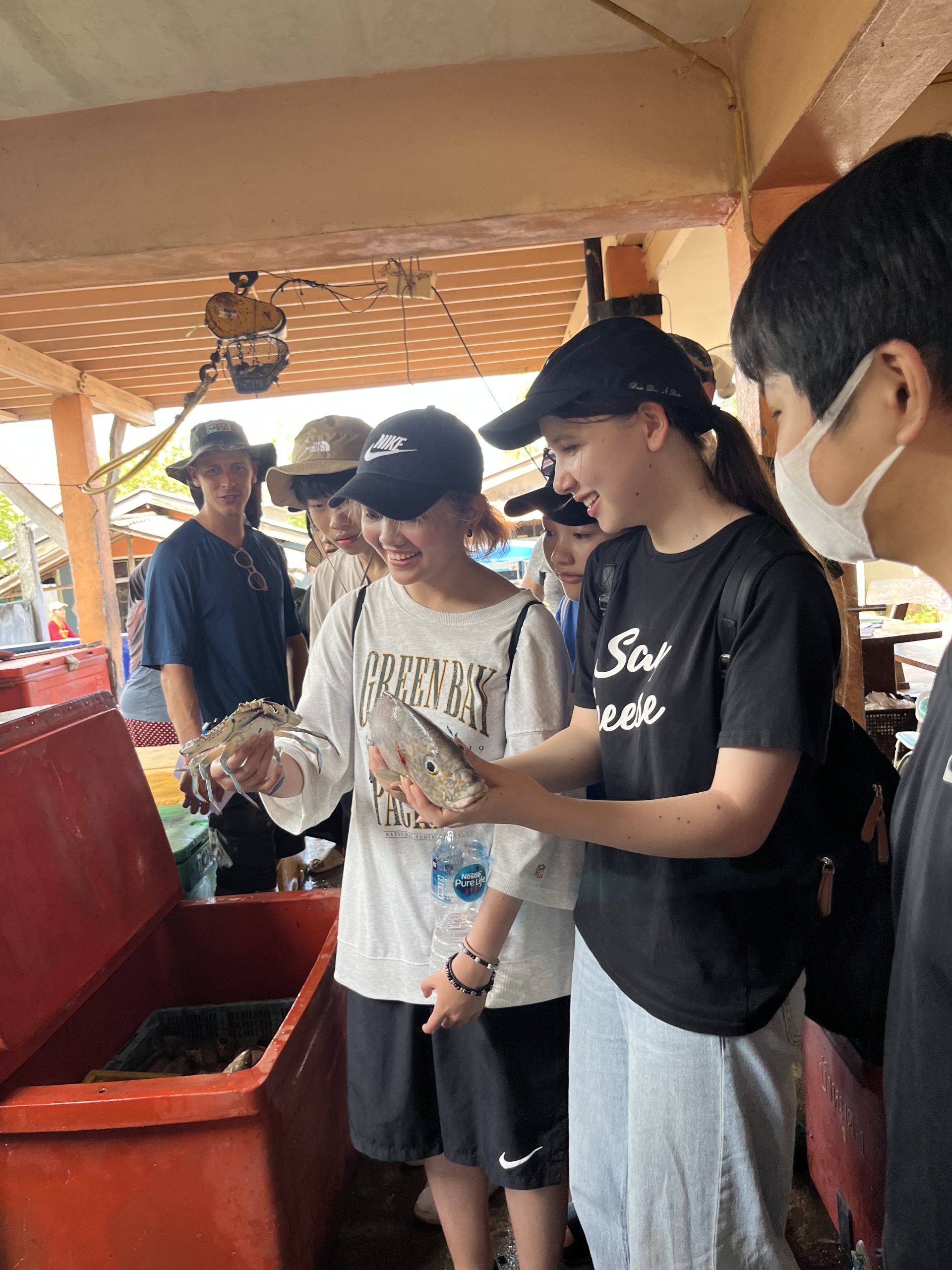 Students examine freshly caught fish near a market stall