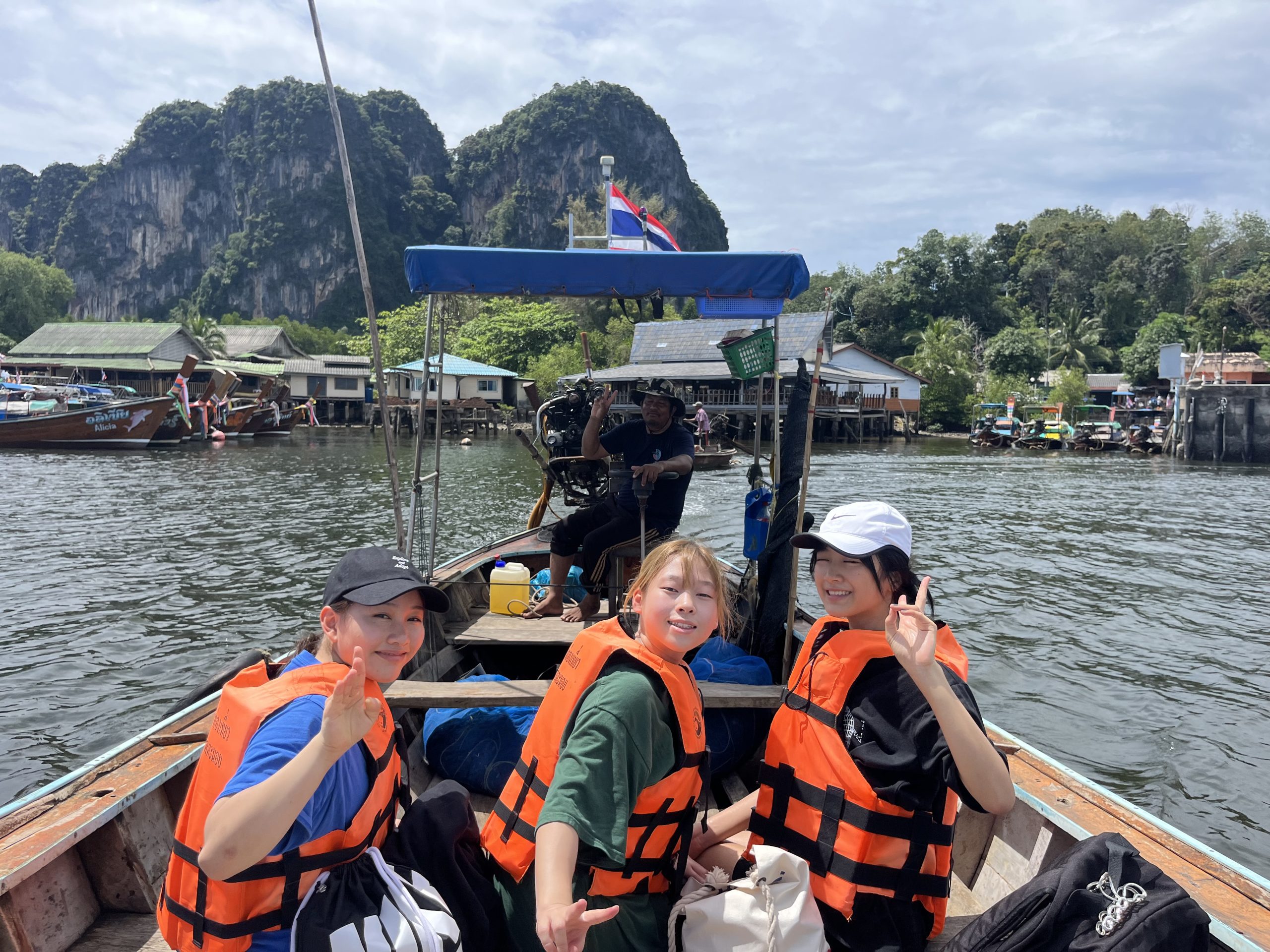Students in life jackets wave from a longtail boat near limestone cliffs in Thailand