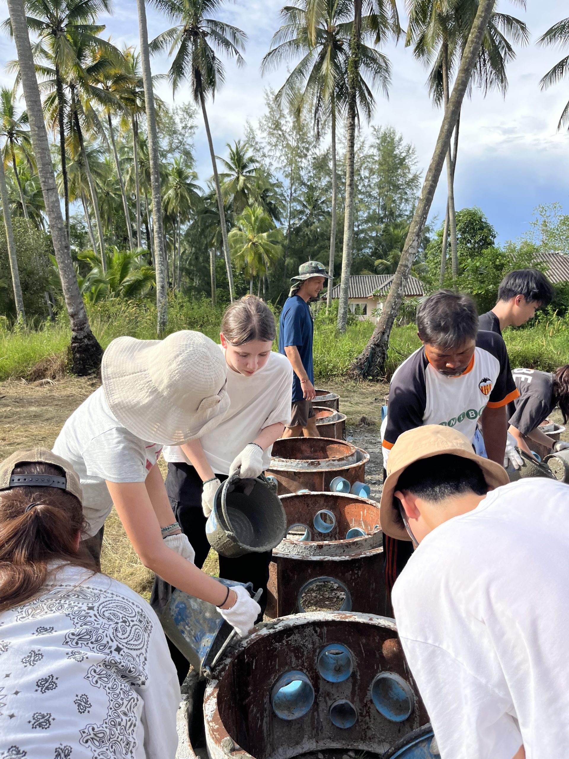 Students and community members build concrete fish houses among palm trees