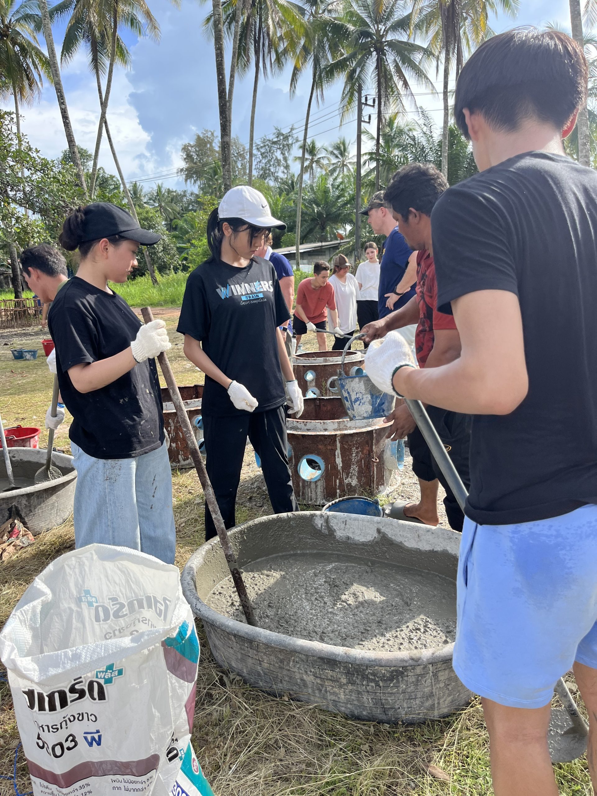 Students in gloves mix concrete in large basins for a community building project