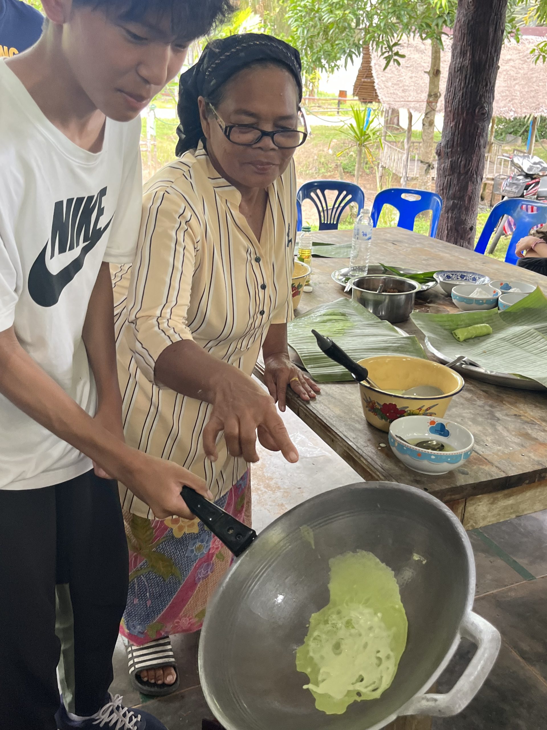 A student learns to prepare batter in a pan with guidance from a local cook