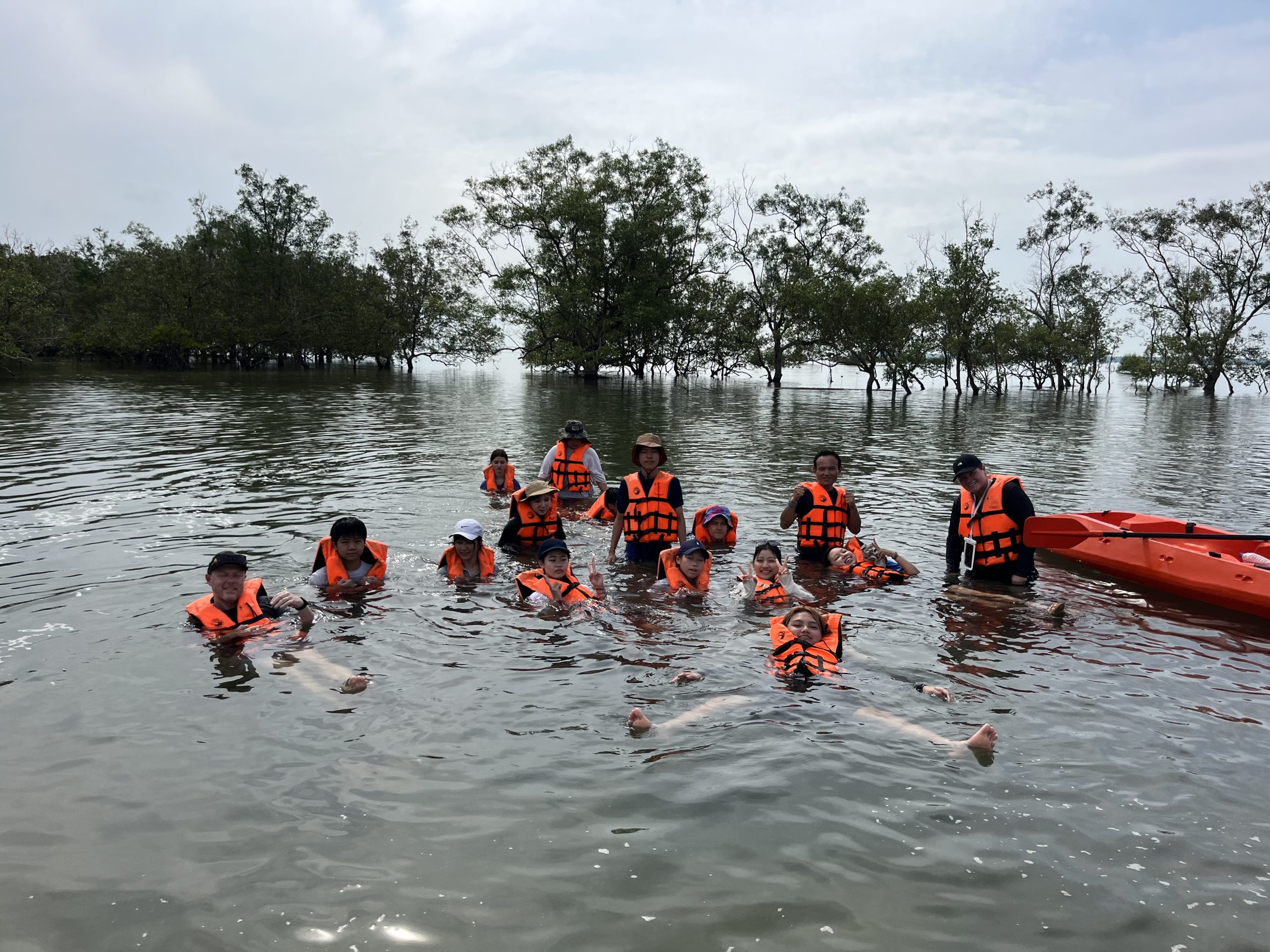 Students in life jackets wade through shallow water near a mangrove forest