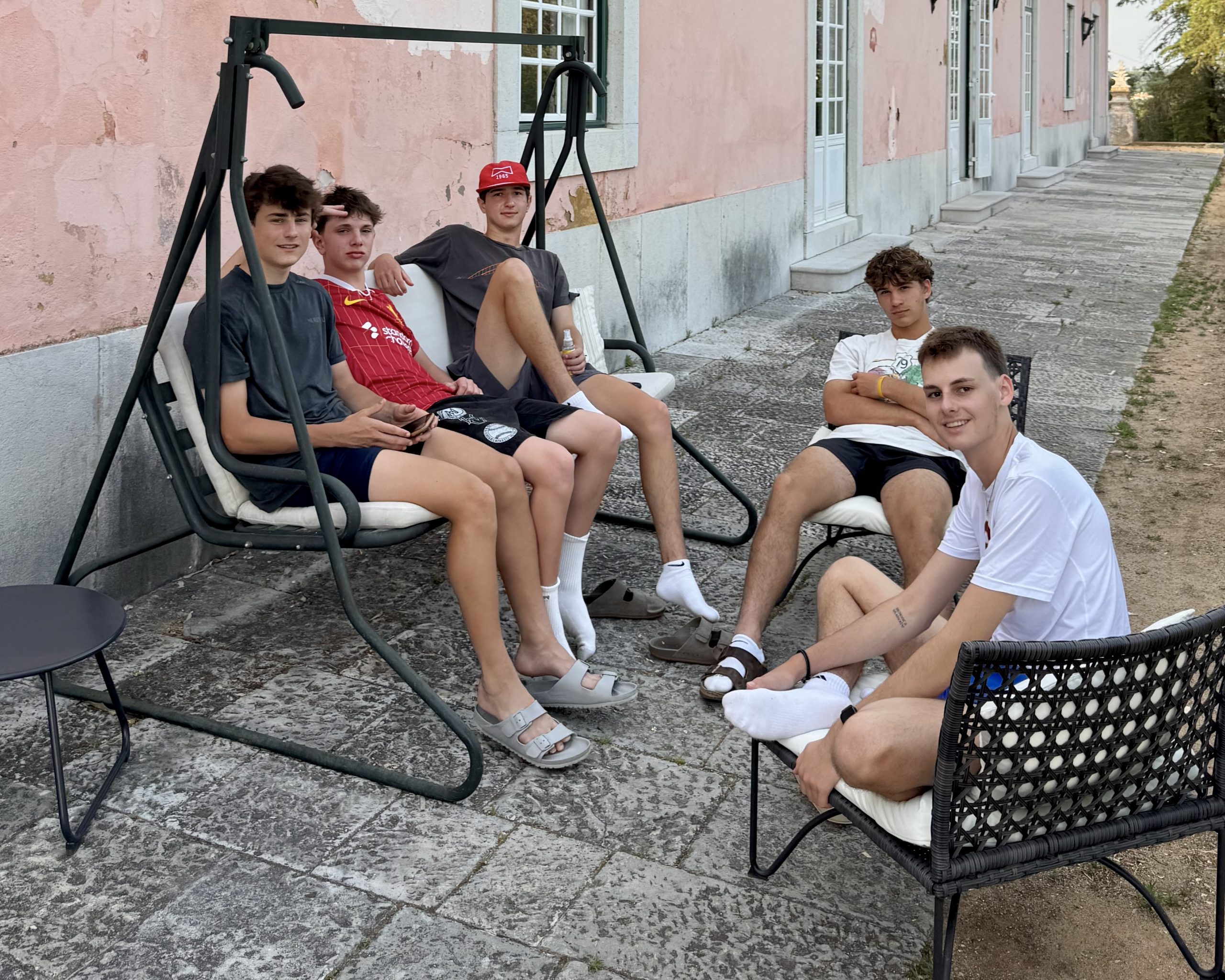 Student travelers relax on outdoor swing chairs along a covered patio