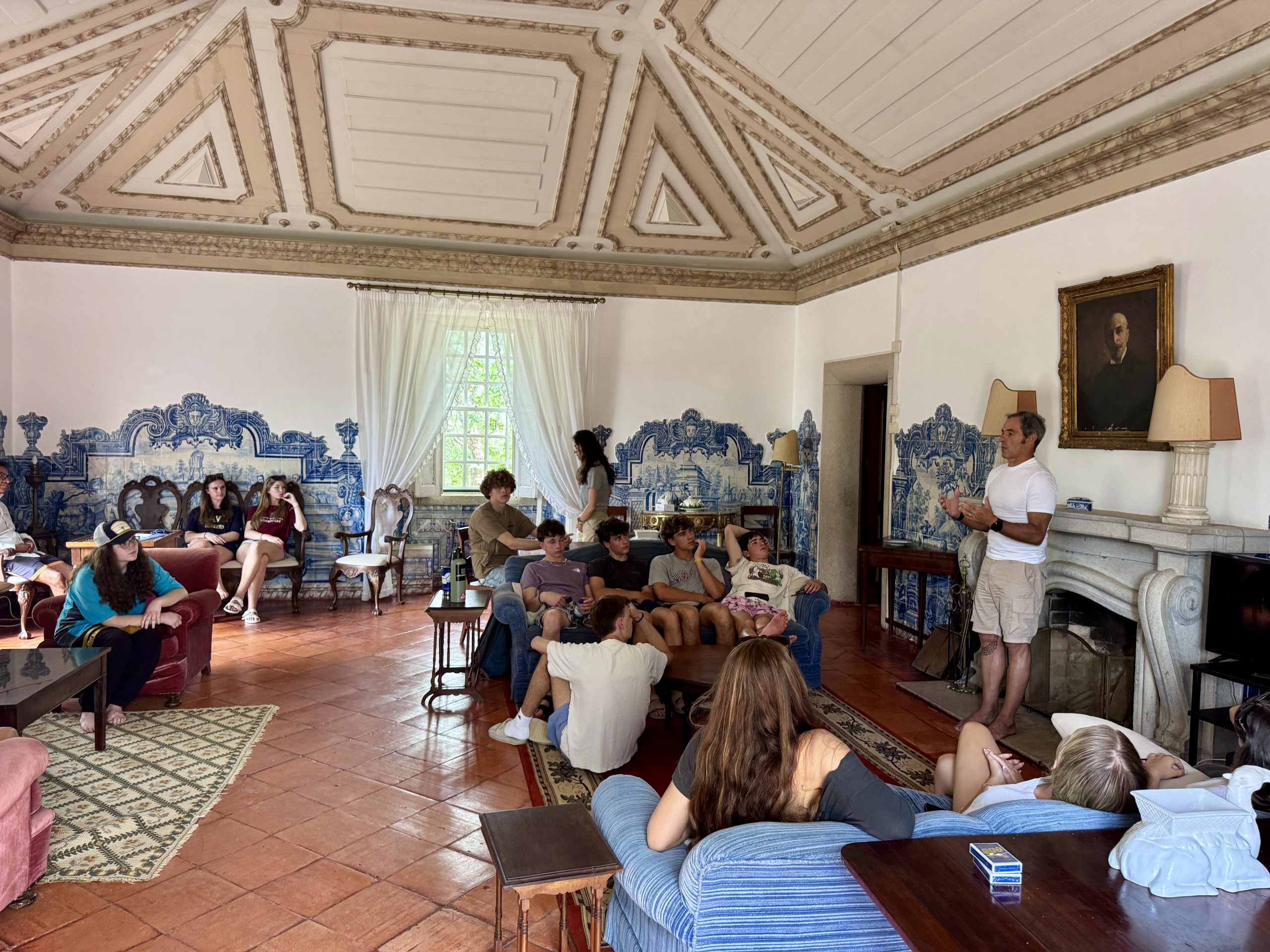 Students sit and listen in a room with blue-and-white tiled walls and an ornate ceiling