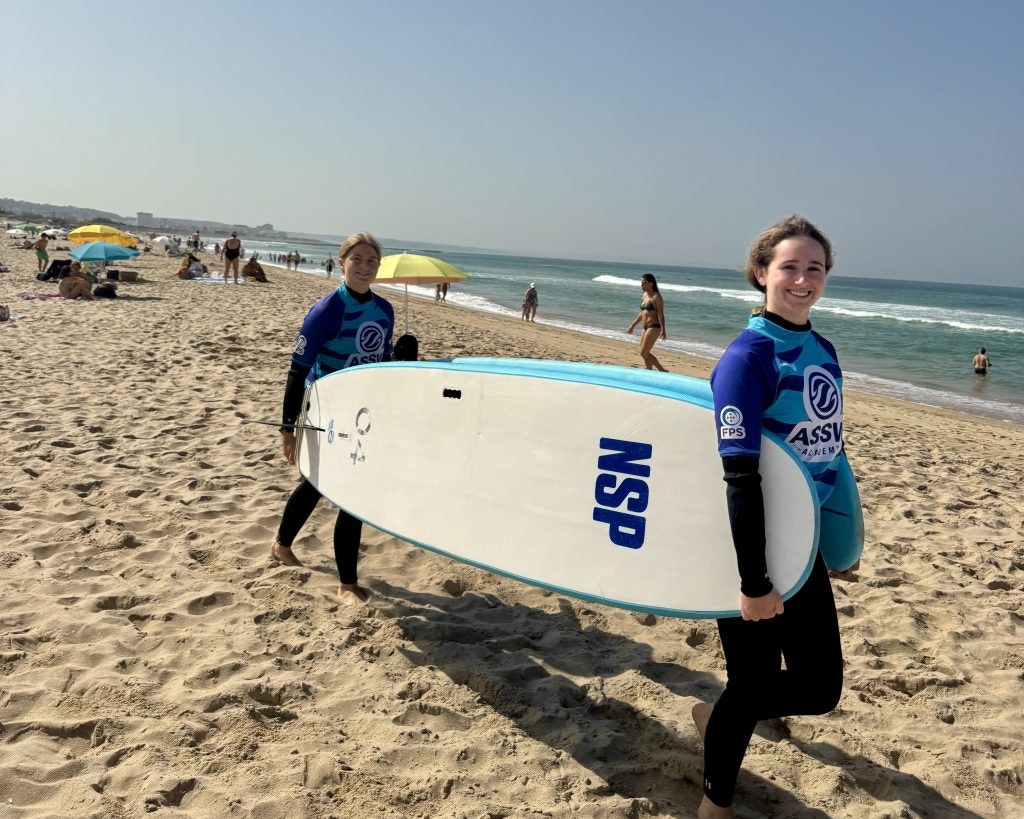 Two students carry a surfboard on a beach during a surf lesson on a teen tour in Portugal and Spain.
