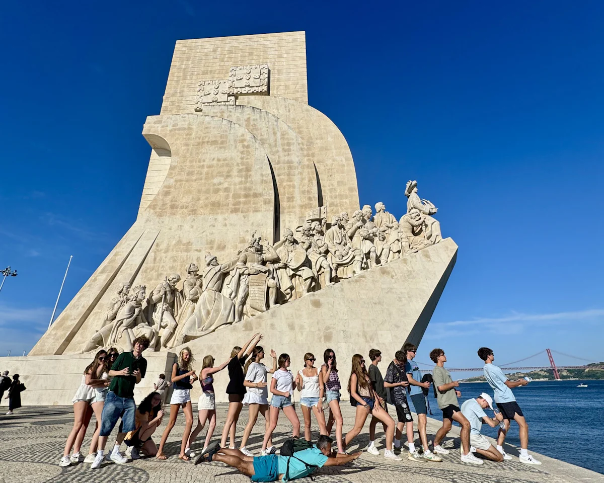 A group of teen travelers lines up along the base of the Monument to the Discoveries on the Lisbon waterfront in Portugal
