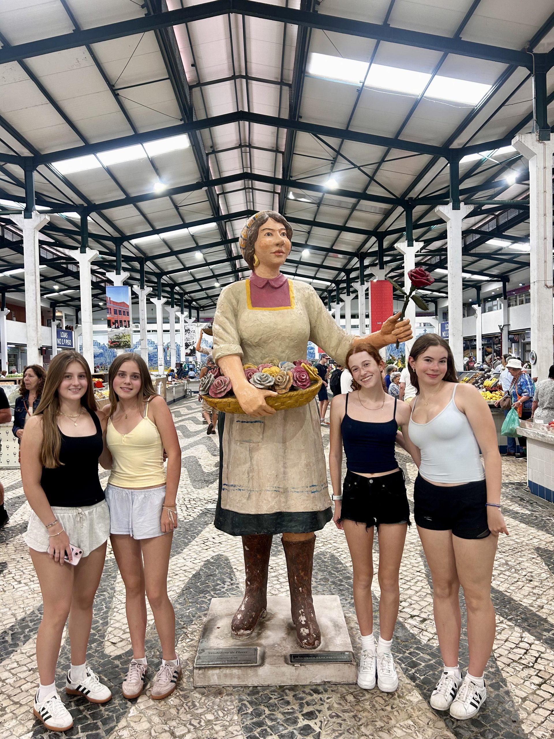 Students pose beside a statue of a market woman inside a covered marketplace