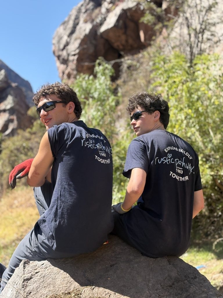 Two students wearing Rustic Pathways t-shirts sitting on a rock in the Sacred Valley in Peru.