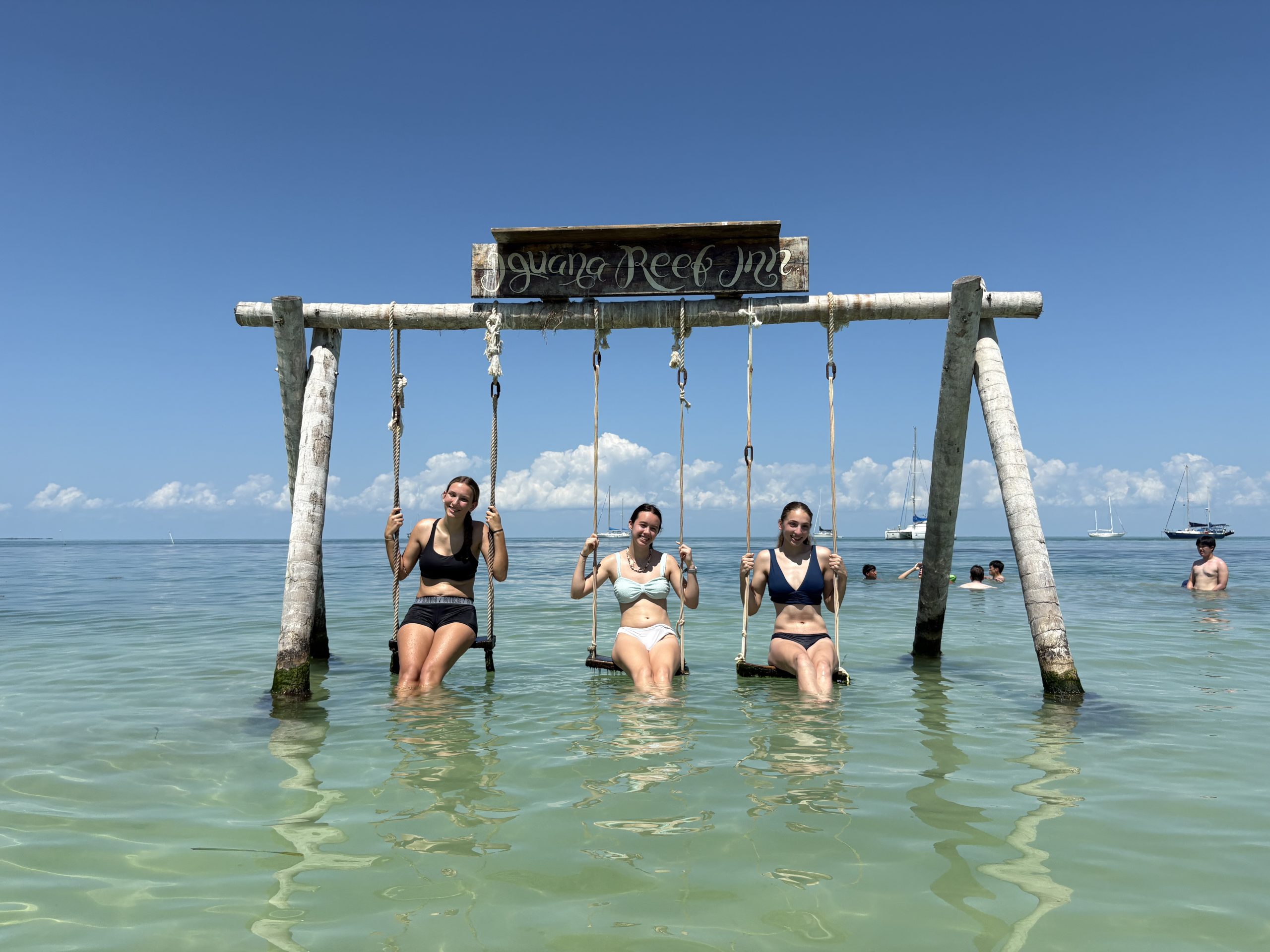 Students sit on swings over shallow turquoise water in Belize