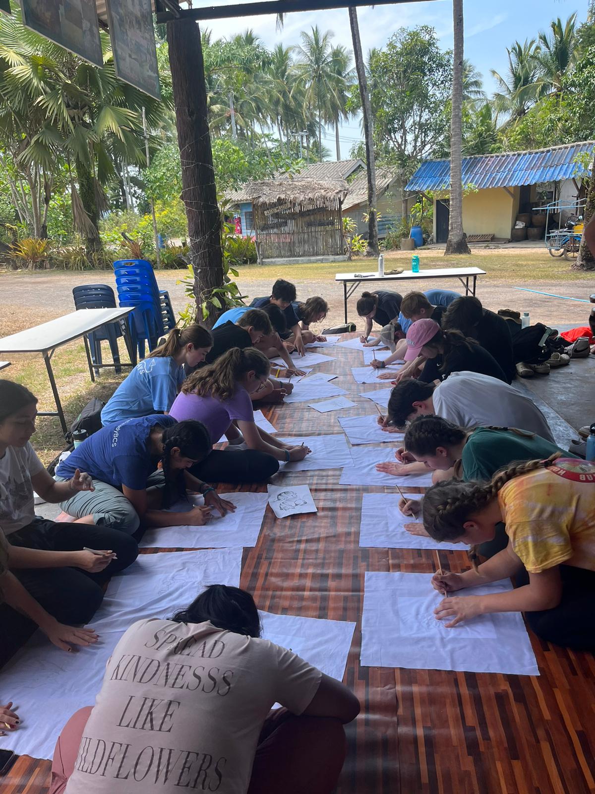 On this school trip, students sit on the floor under a shaded pavilion, drawing on large sheets of paper