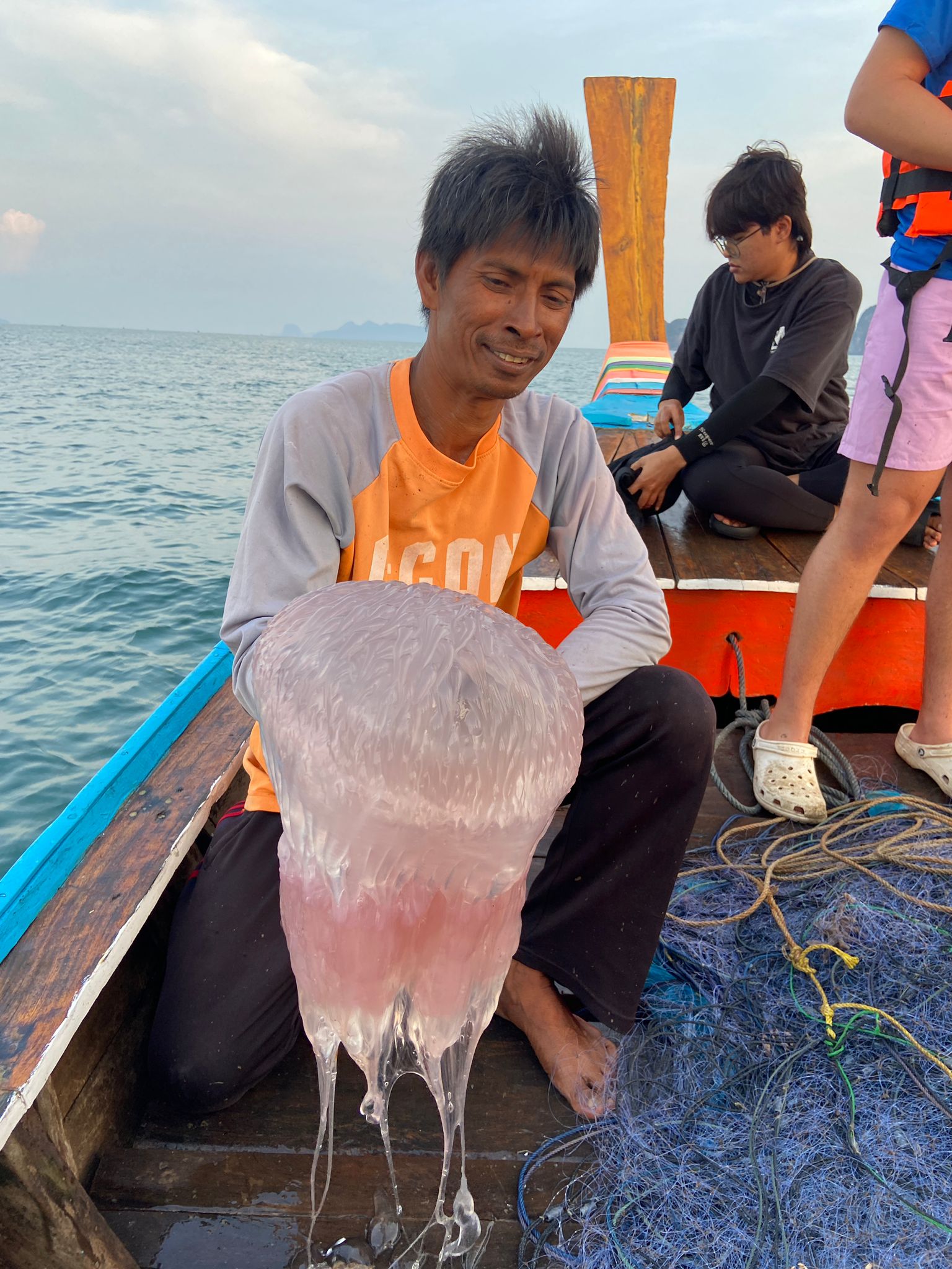 A boat guide holds a large jellyfish aboard a longtail boat as students look on