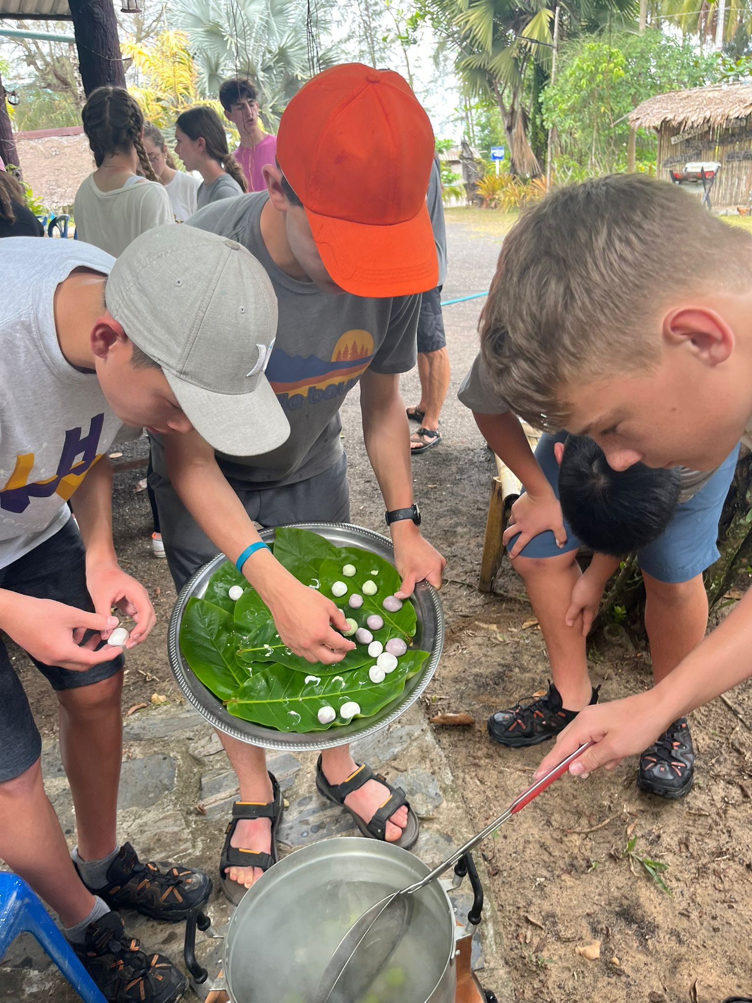 Students gather around a tray of leaves and small ingredients during a cooking activity