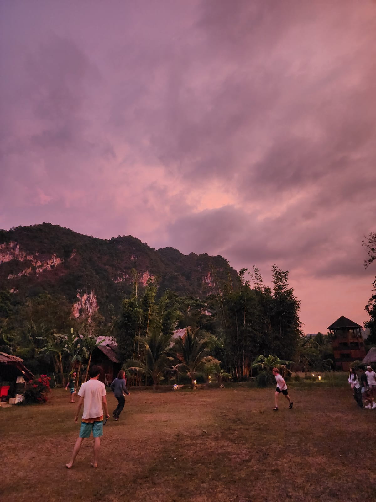 Students play in an open field beneath limestone karsts at dusk