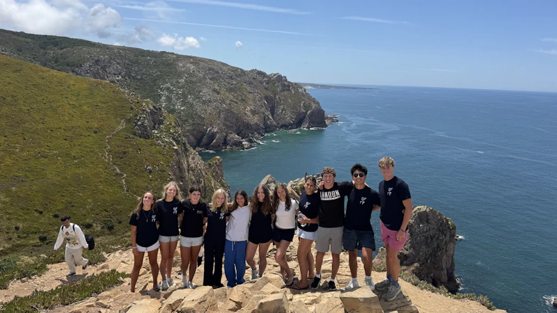 A group of teen travelers poses on a clifftop above the Atlantic Ocean in Portugal