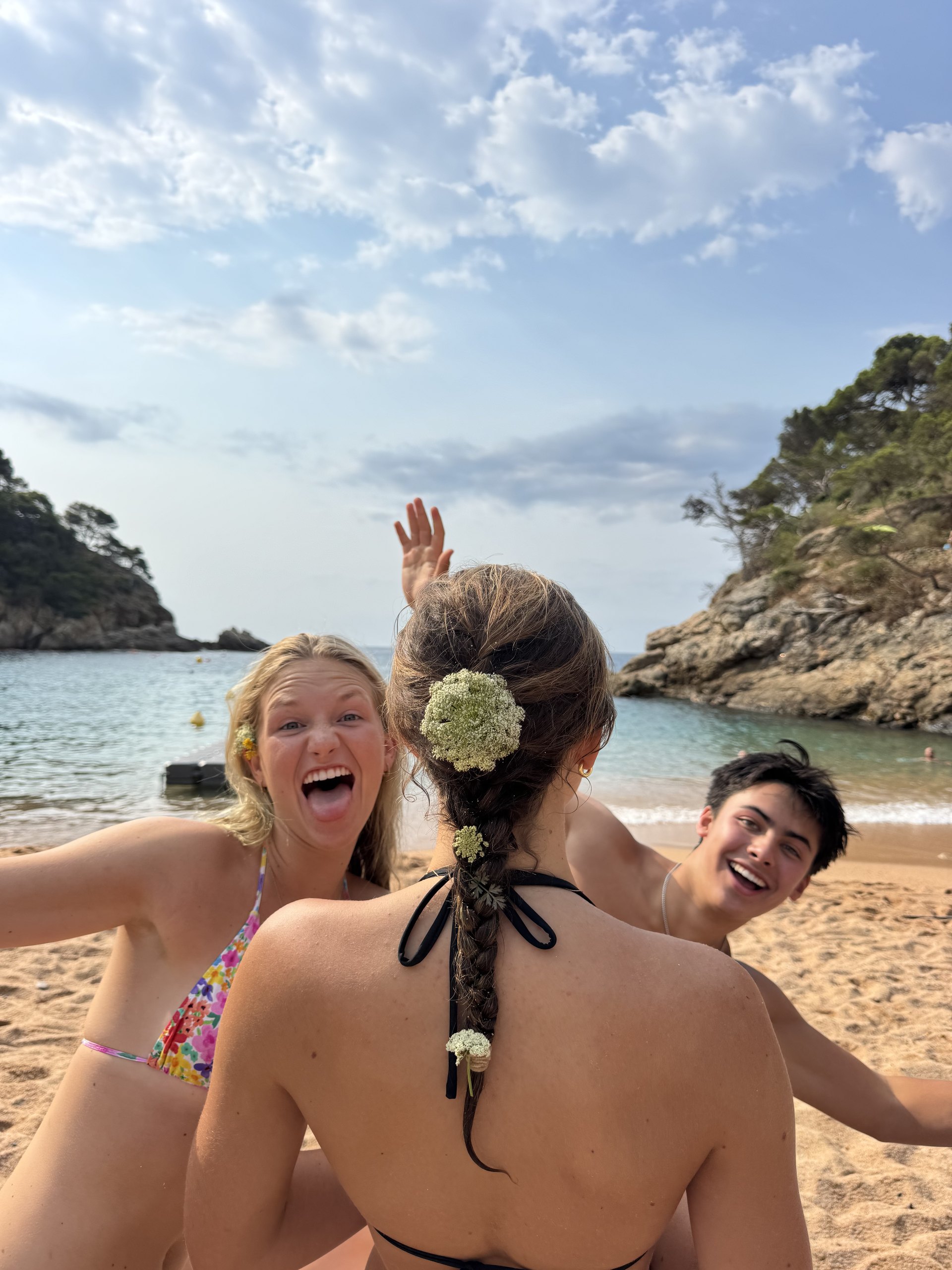 Three teen travelers laugh and pose for a selfie on a beach in a rocky cove