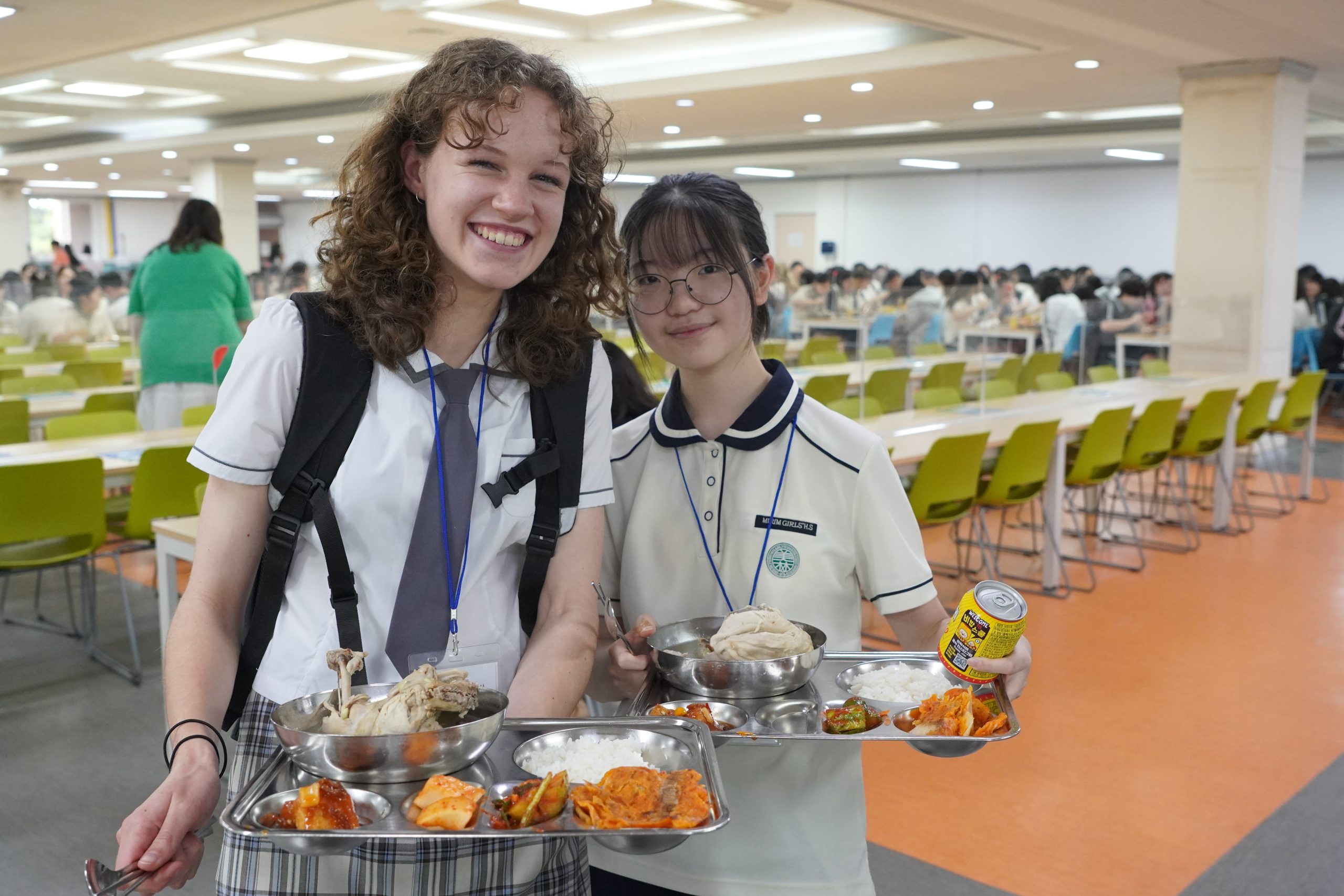 Student travelers smile while holding trays of Korean food in a school cafeteria