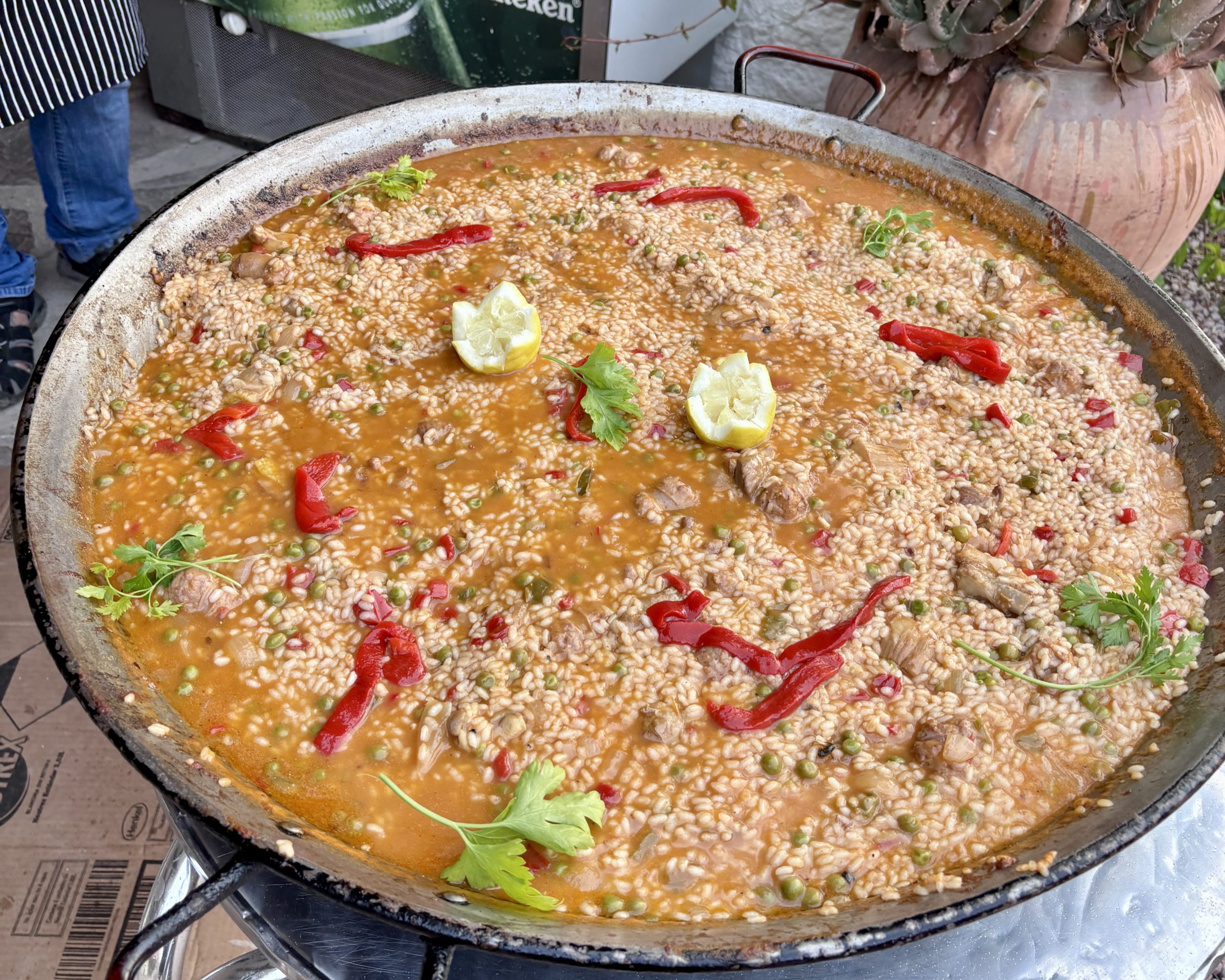 A large paella pan simmers with rice, peppers, meat, and lemon garnish