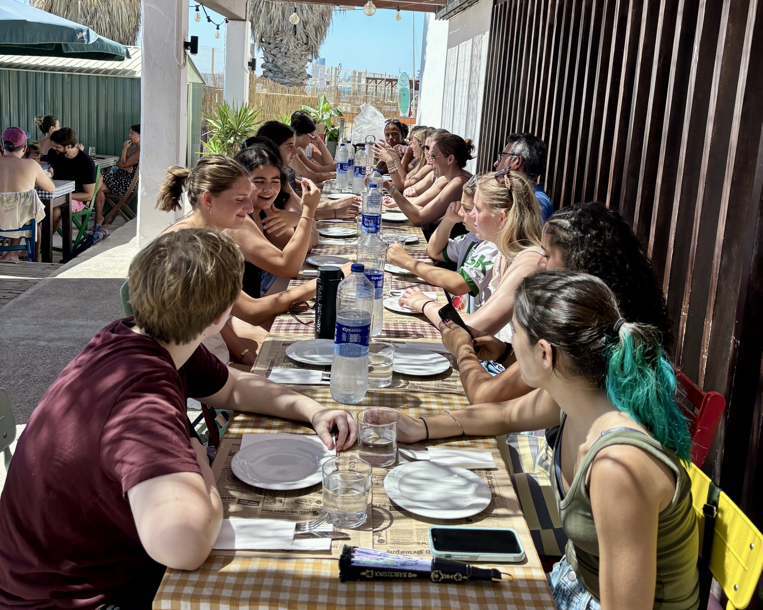Students share a meal at a long outdoor table set with water bottles and plates