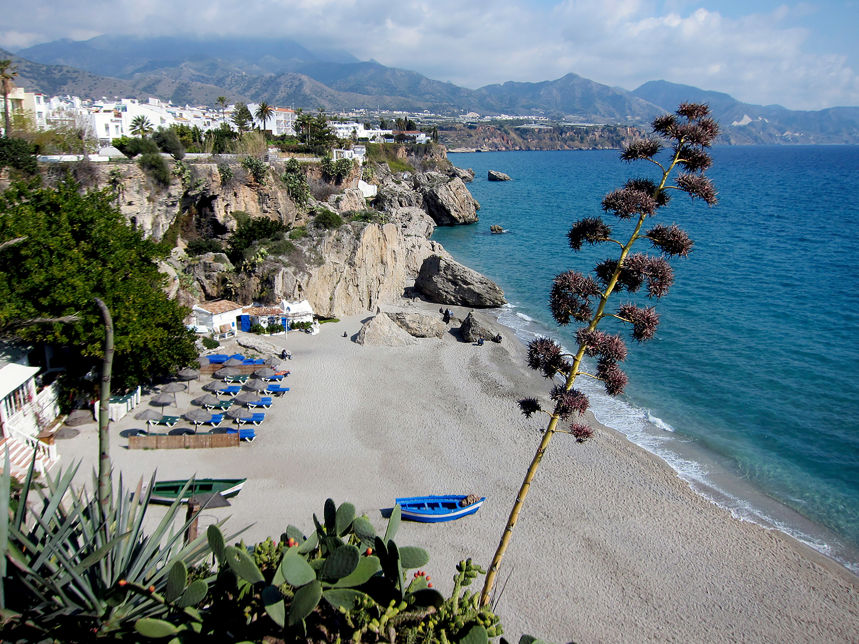 A coastal beach and cliffs curve along the Mediterranean below a whitewashed hillside town