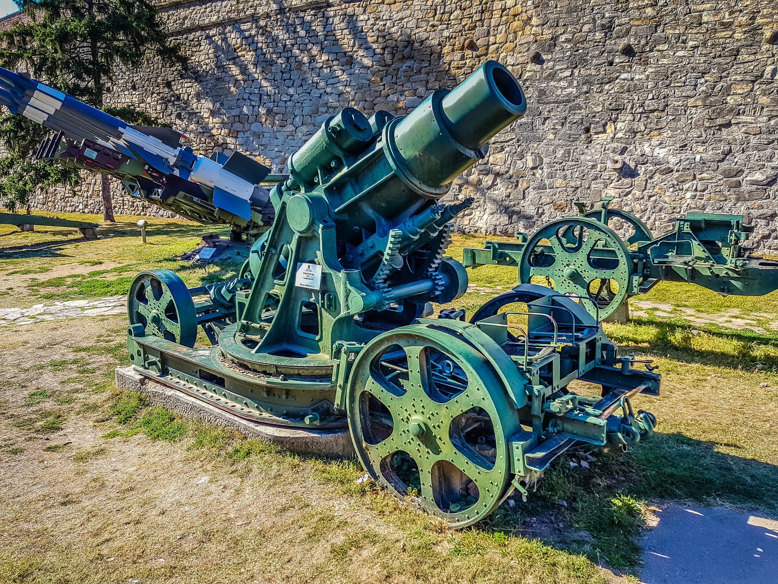 A weathered green cannon from an old artillery collection sits on a lawn at a fortress museum.