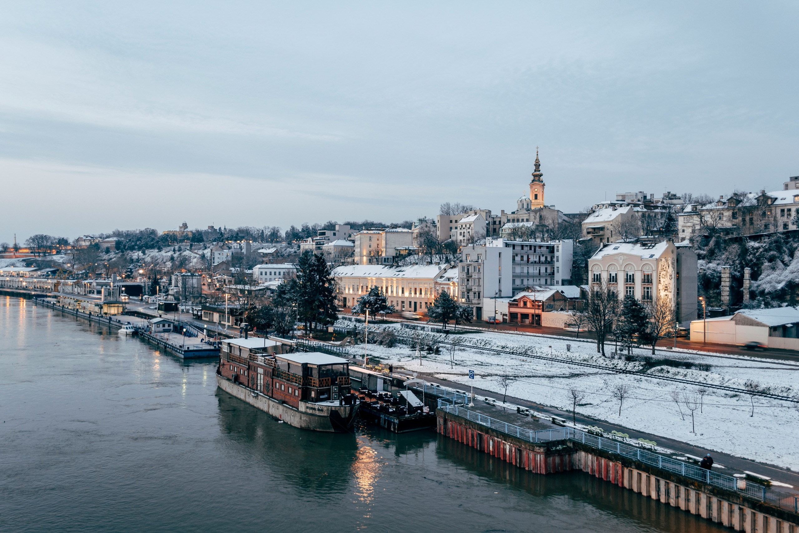 Historic riverside buildings line a snow-dusted embankment in a European capital.