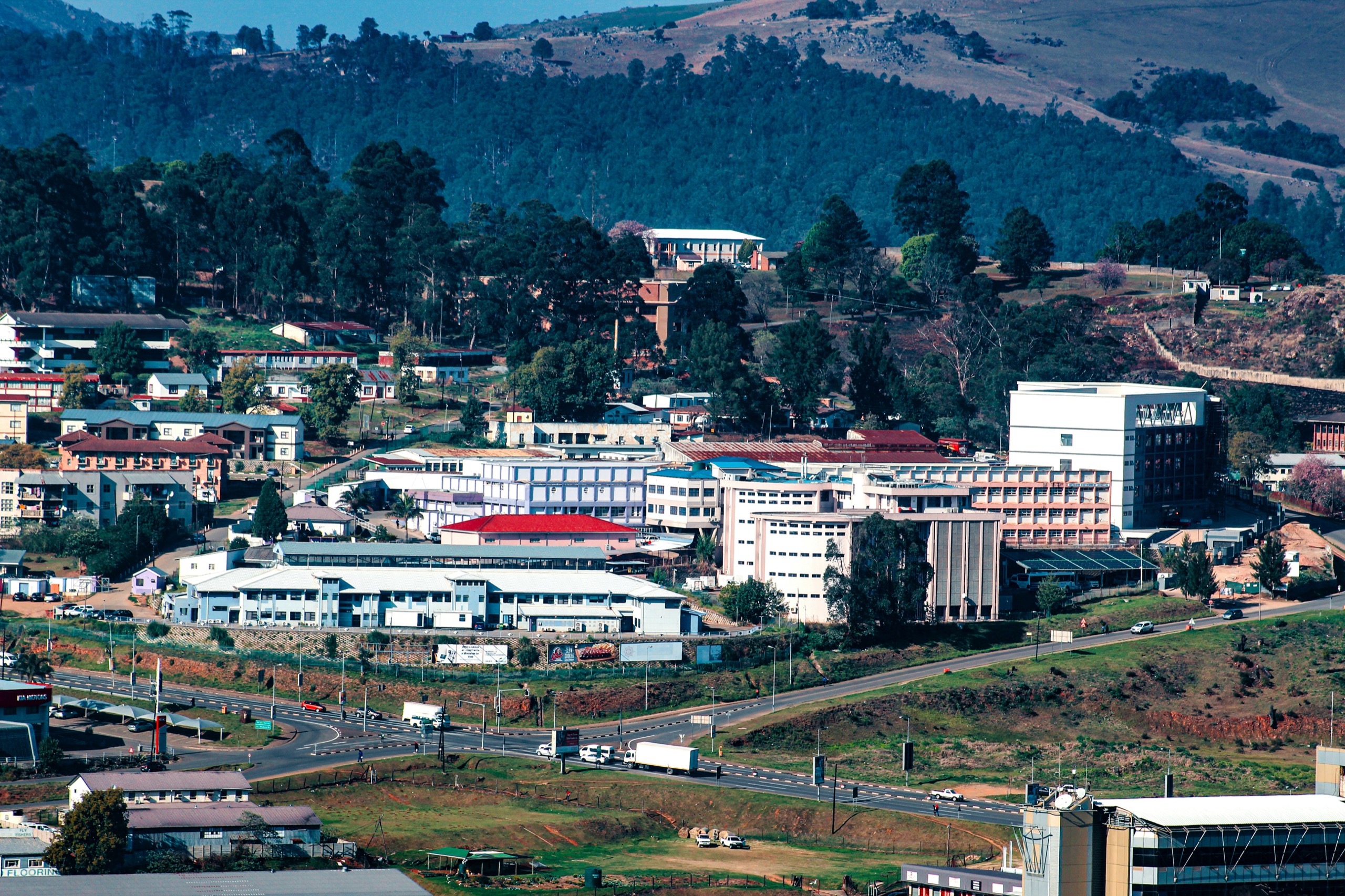 A hillside city of low buildings and a few office blocks, ringed by wooded slopes, with a road curving through it.