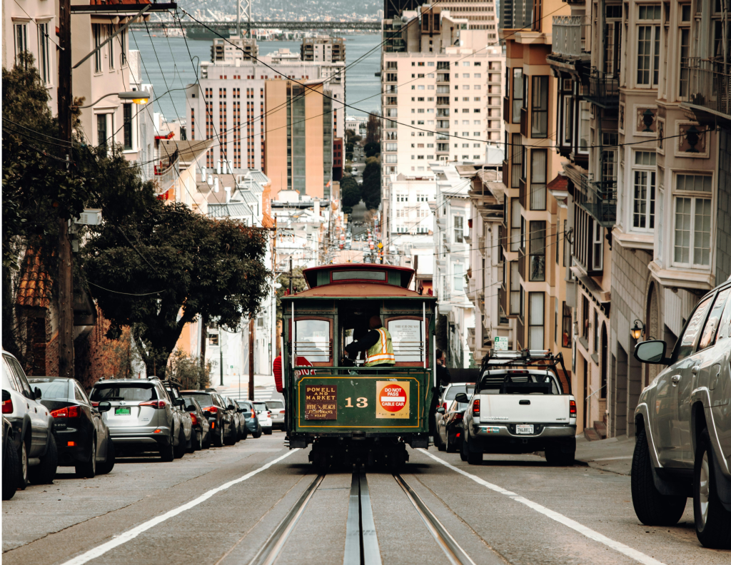 A San Francisco cable car descending a steep street with the city and water in the background.