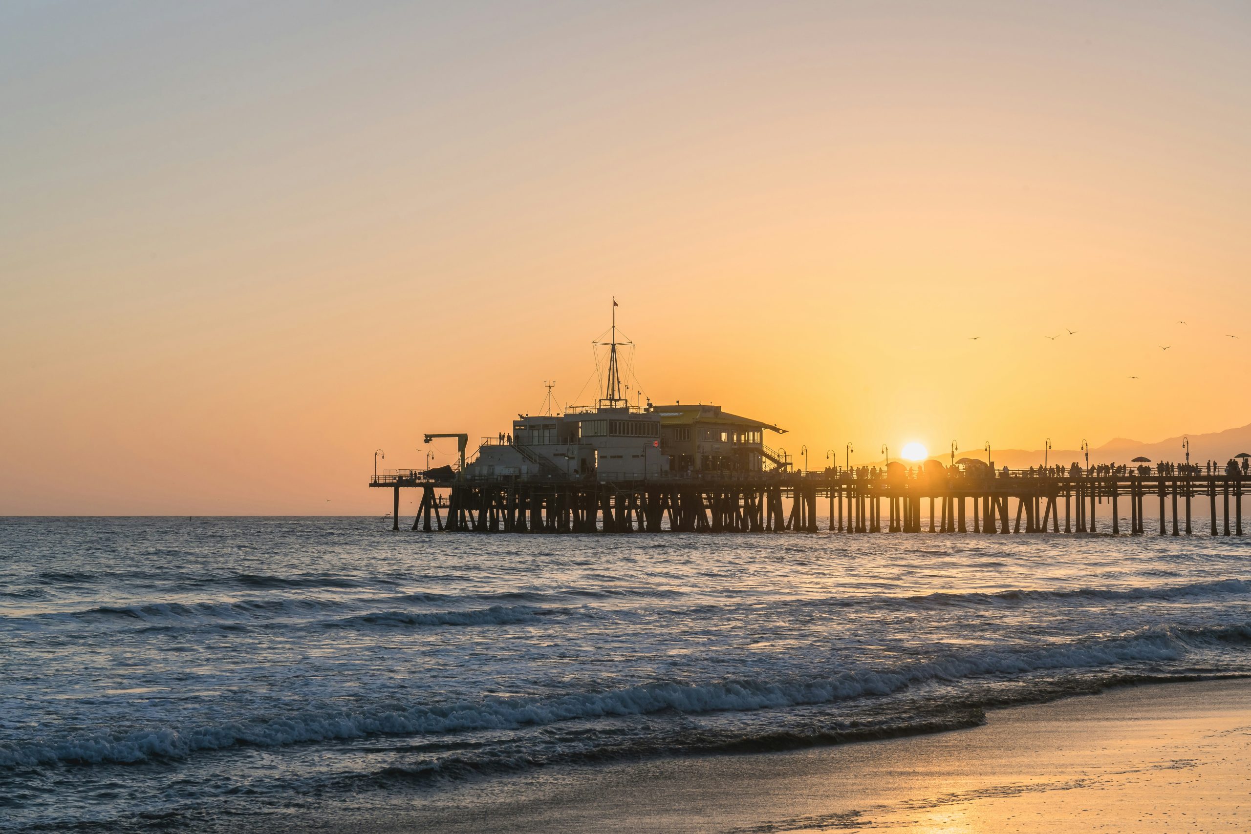 A school trip stops at Santa Monica Pier as the sun sets and waves roll onto the beach