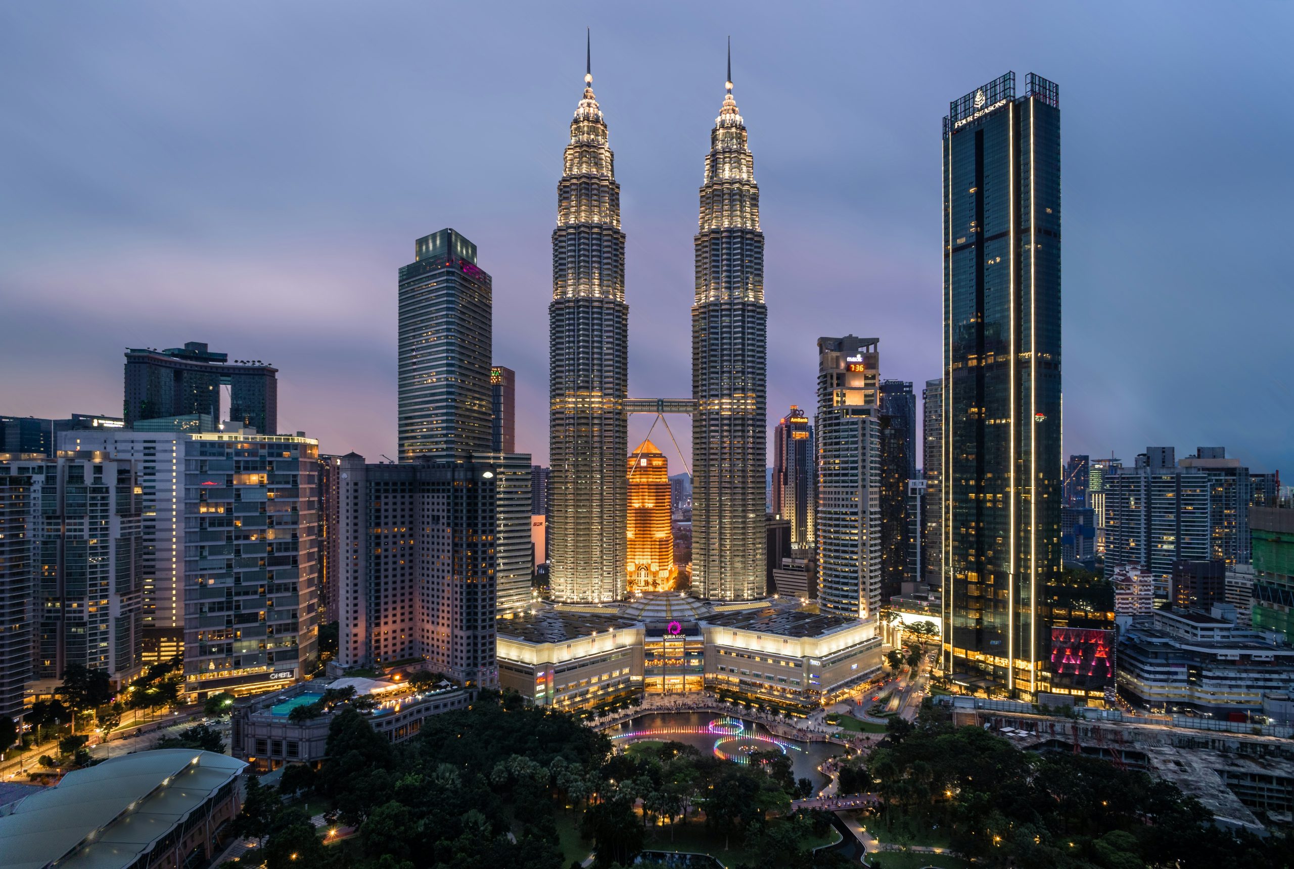 The Petronas Twin Towers rise above the Kuala Lumpur skyline at dusk, lit gold against a purple sky.