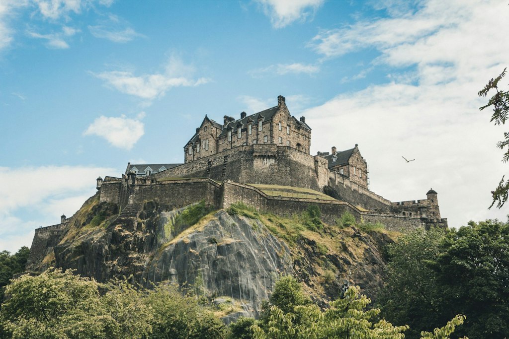 Landscape picture of Edinburgh Castle. Hill is grassy and sky is clear and blue. 