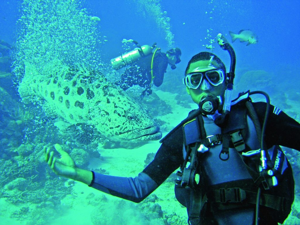 A teen SCUBA diver in diving gear with a large fish in the background during a learn to dive abroad student travel program.