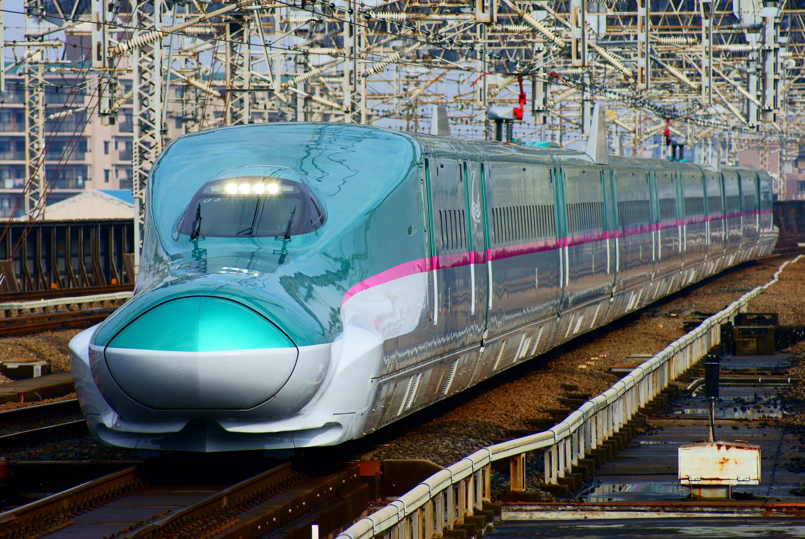 A green and white shinkansen bullet train approaches on elevated tracks