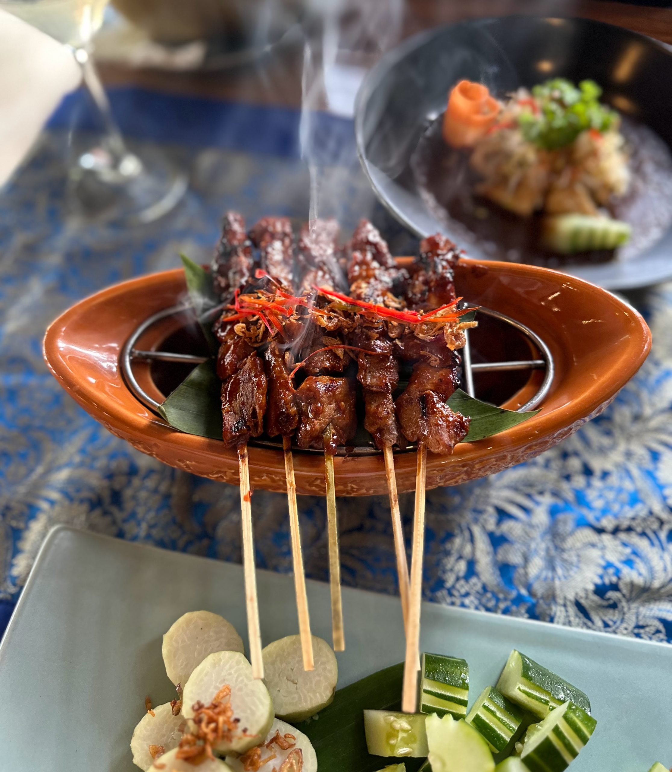 Grilled meat skewers served with cucumber and rice, steaming on a hot plate in Bali.