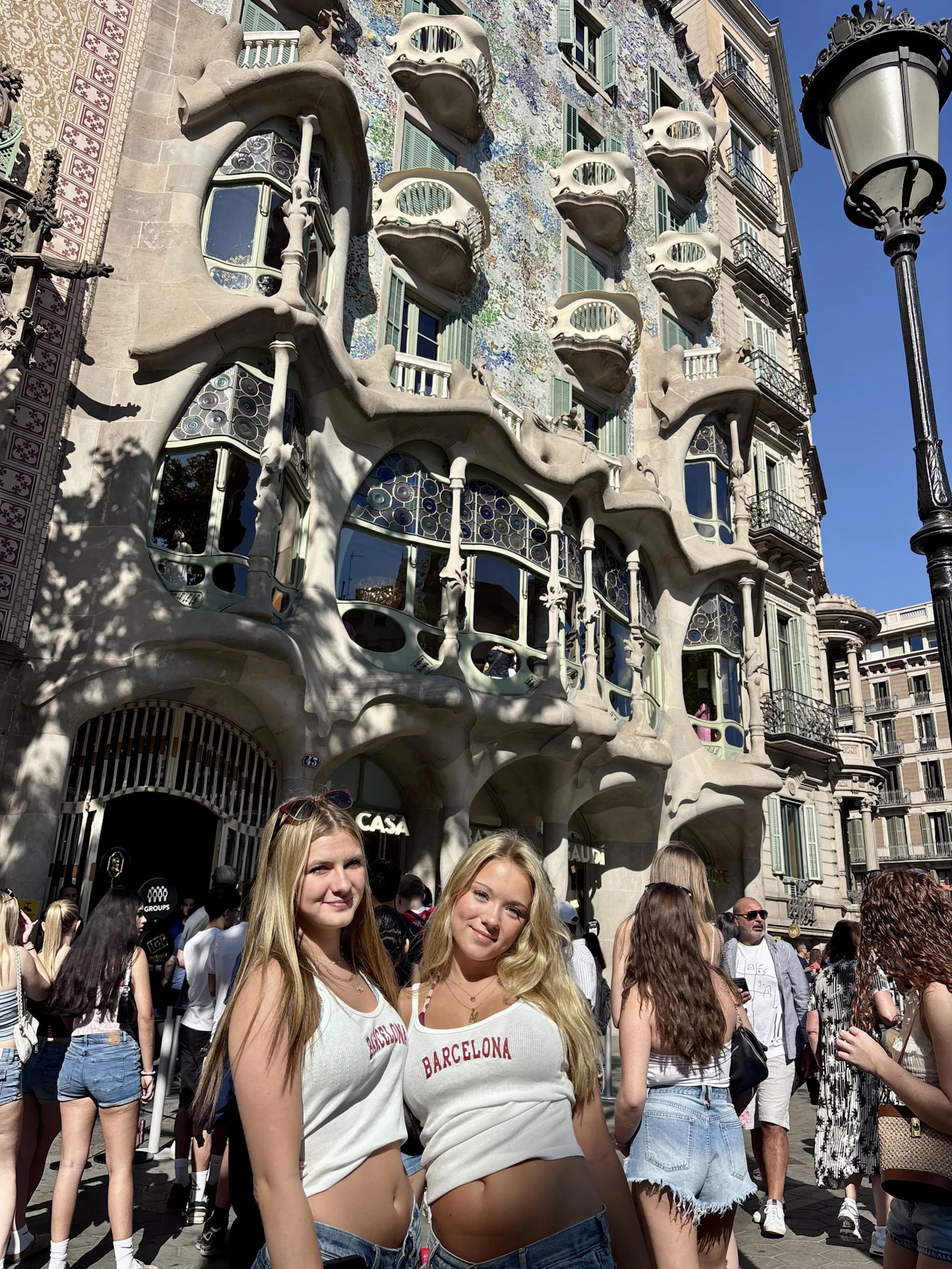 Two teen travelers stand on the Passeig de Gràcia in Barcelona, Spain, in front of the curved balconies of Casa Batlló
