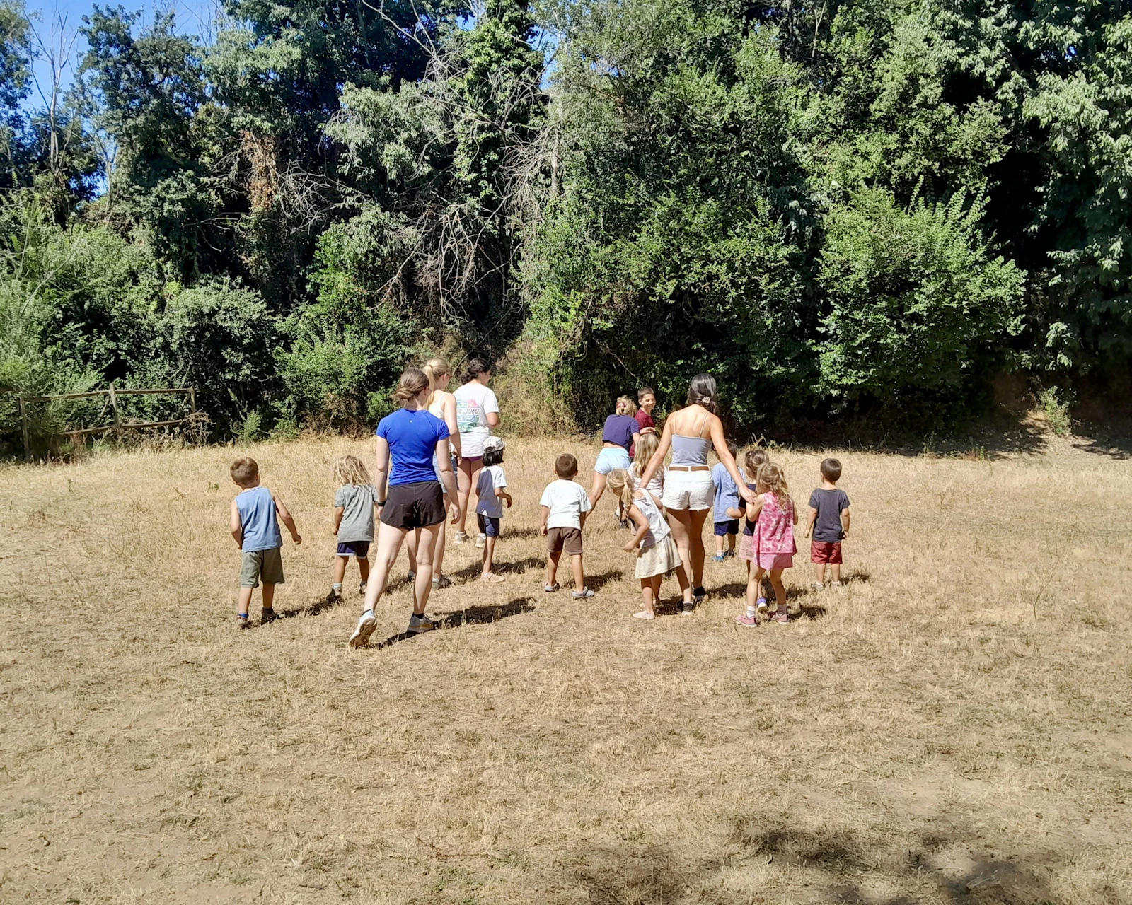 Teen travelers walk across a dry meadow with a group of young local children in rural Spain