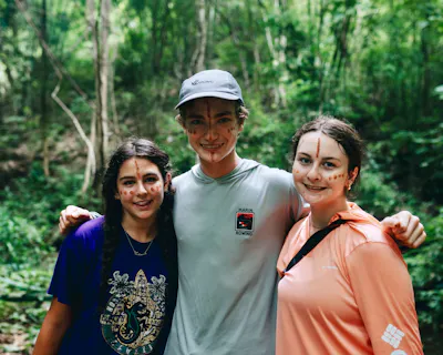 Three travelers with painted face markings standing arm in arm on a jungle trail in northern Thailand