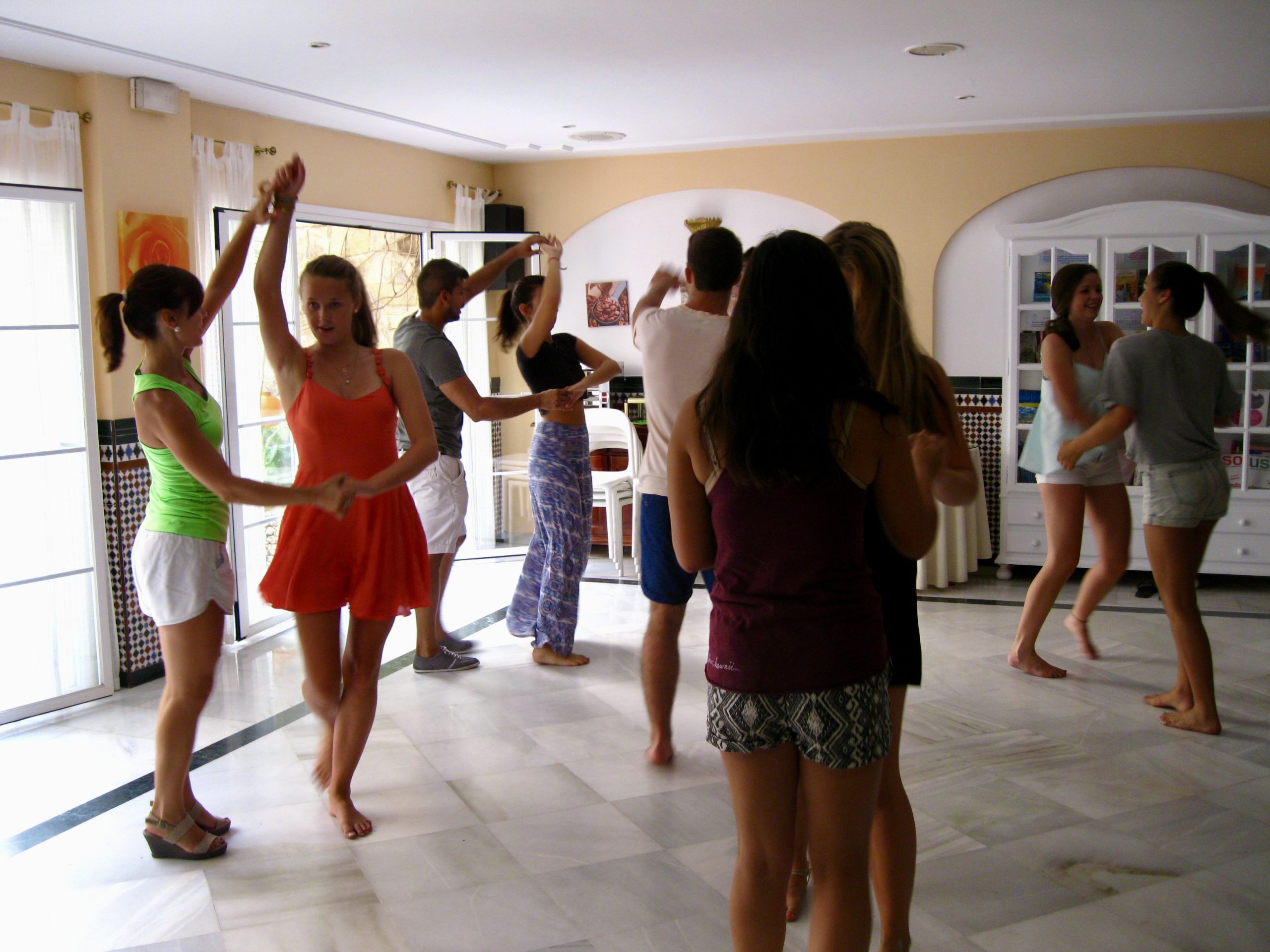 Students pair up to practice flamenco dance steps in a sunlit room
