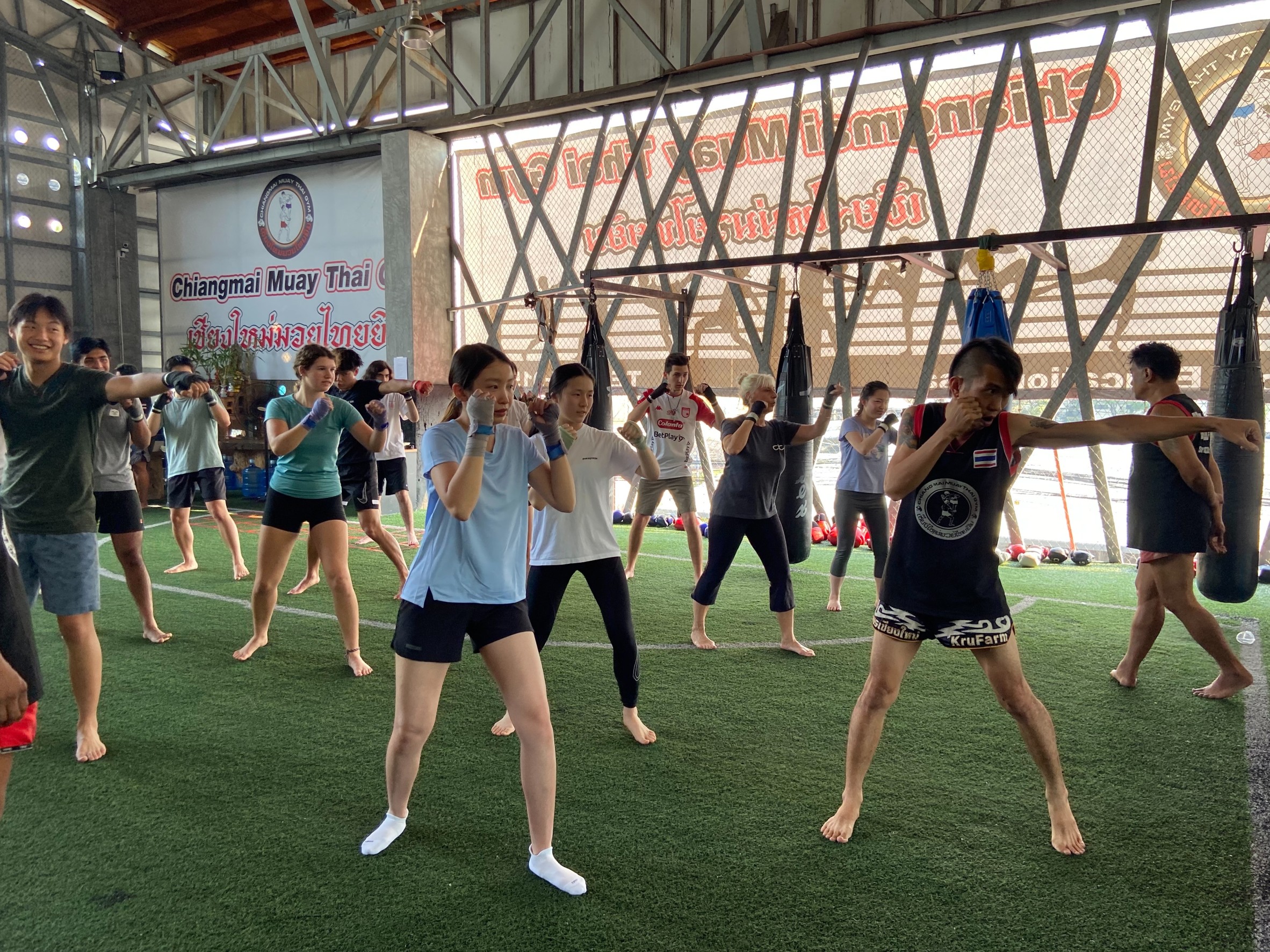 Students practice Muay Thai boxing stances on a turf gym floor at Chiangmai Muay Thai