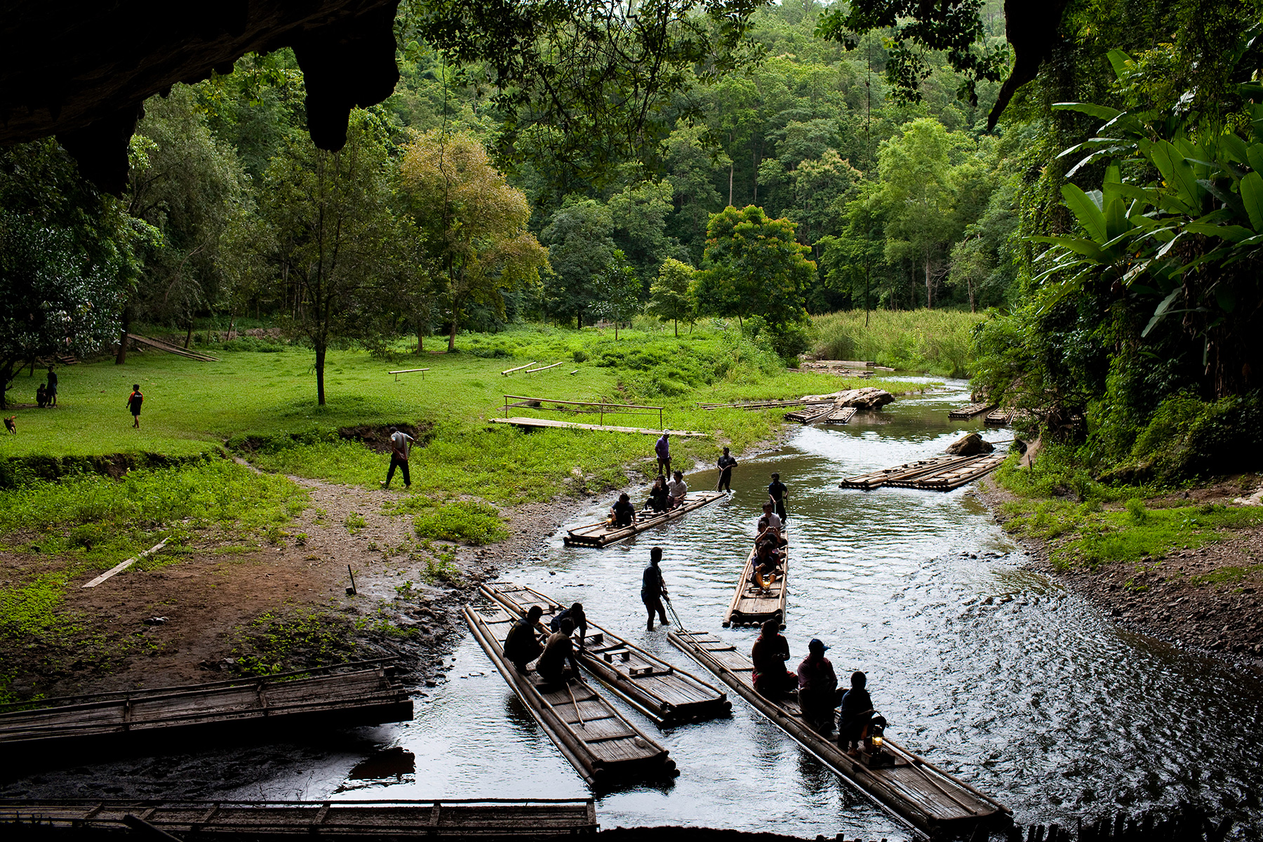 Bamboo rafts carry passengers along a shallow river near a cave entrance in Thailand