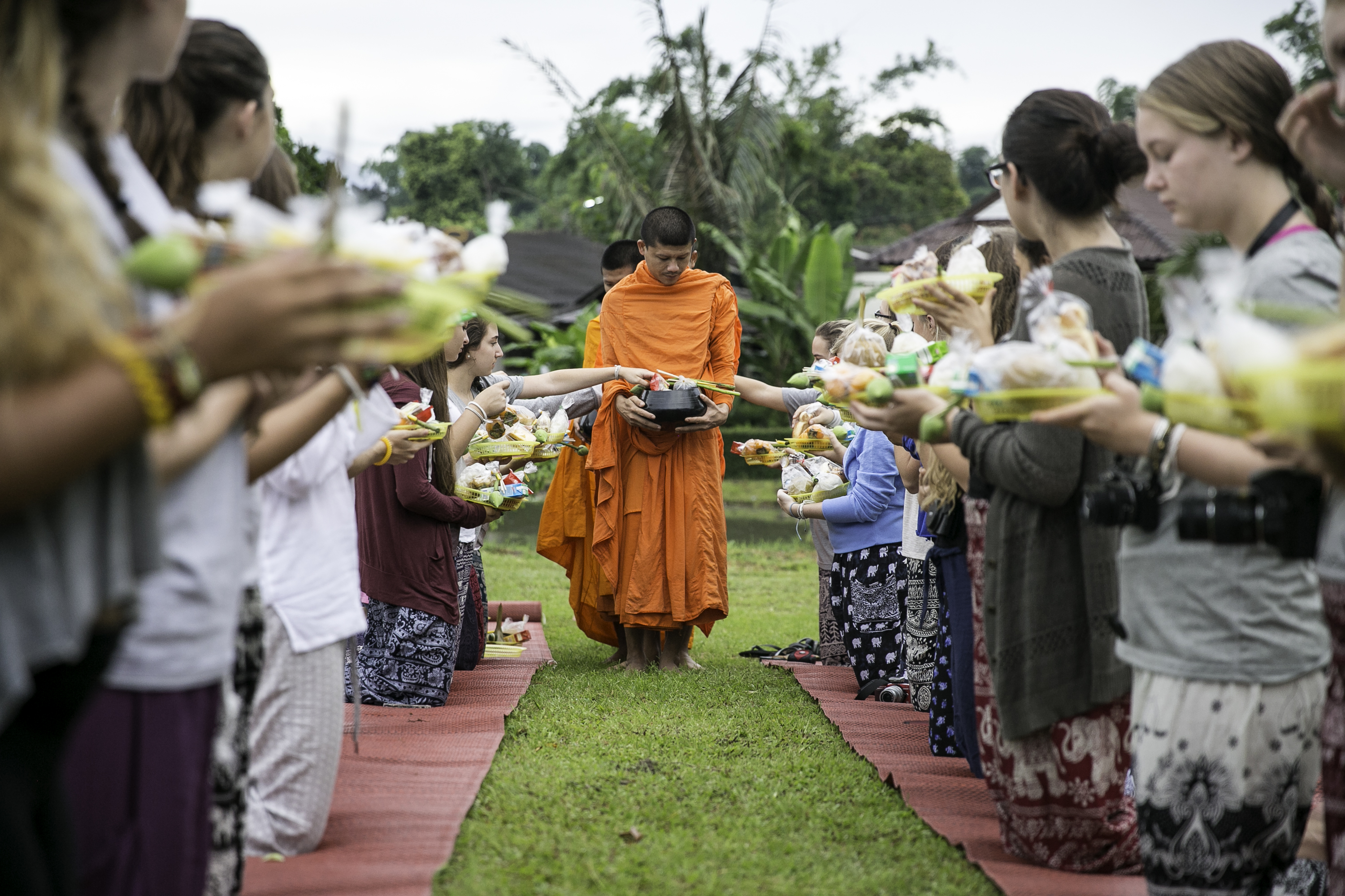 Students line a path offering alms to a Buddhist monk in Thailand
