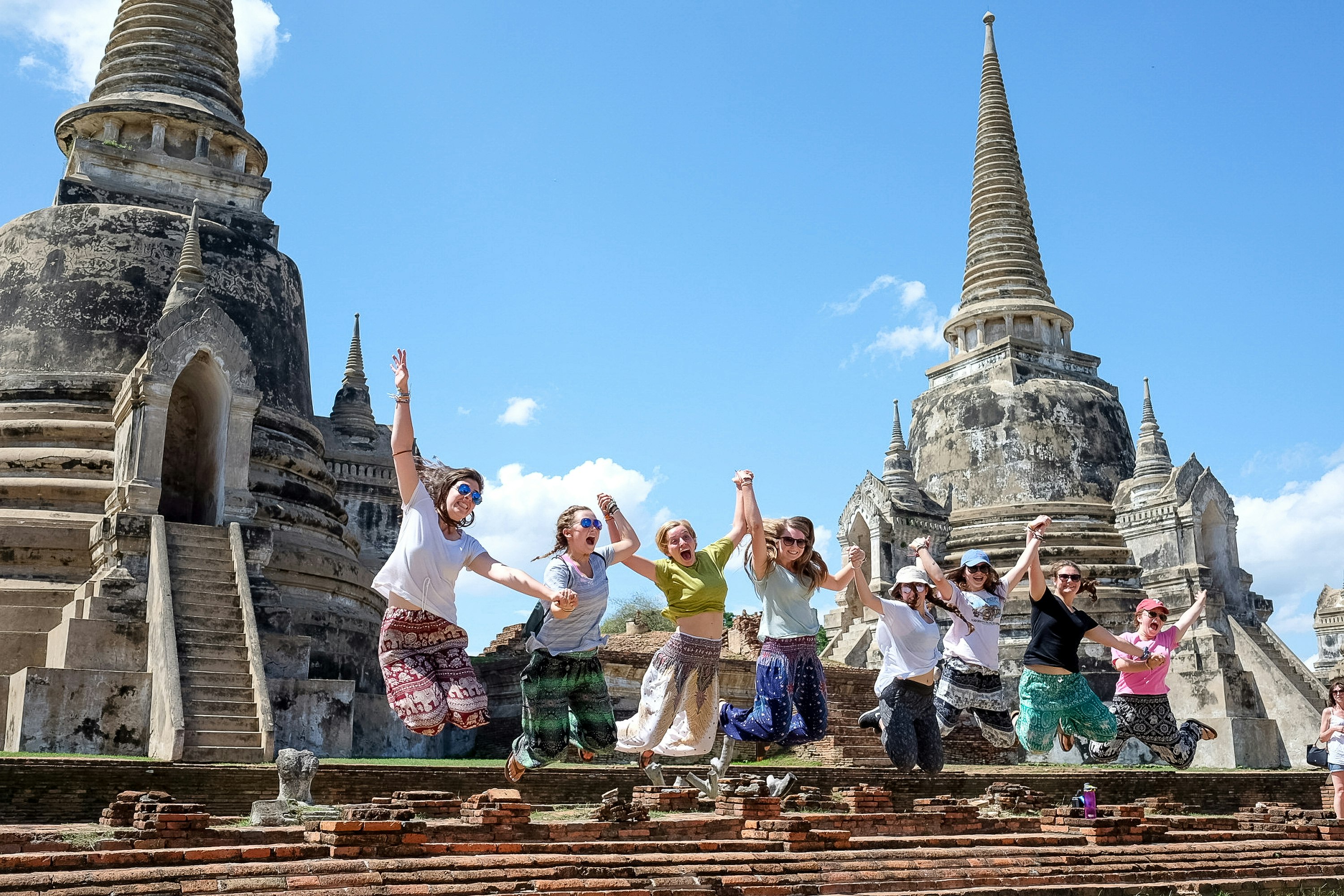 Group of students jumping for a photo in front of a temple in Thailand. 