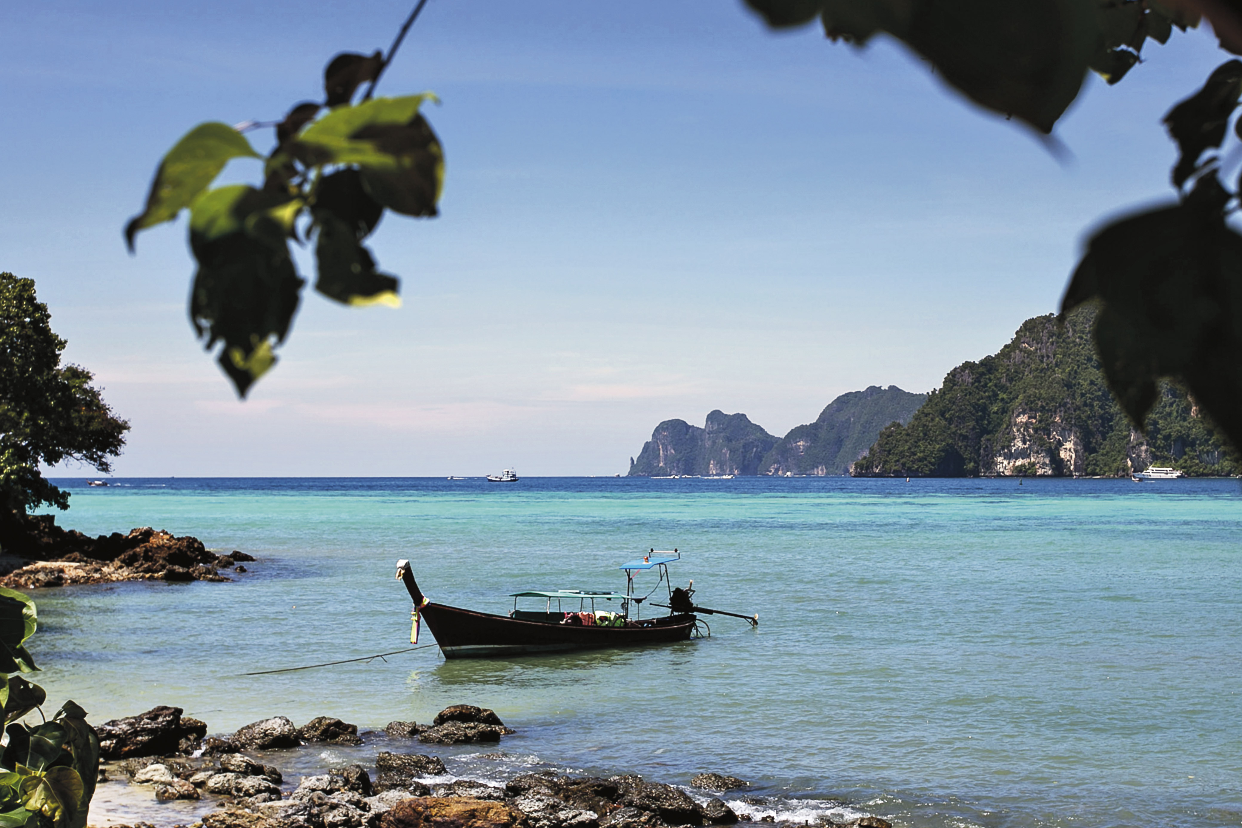 A longtail boat anchored near limestone cliffs along Thailand's coast