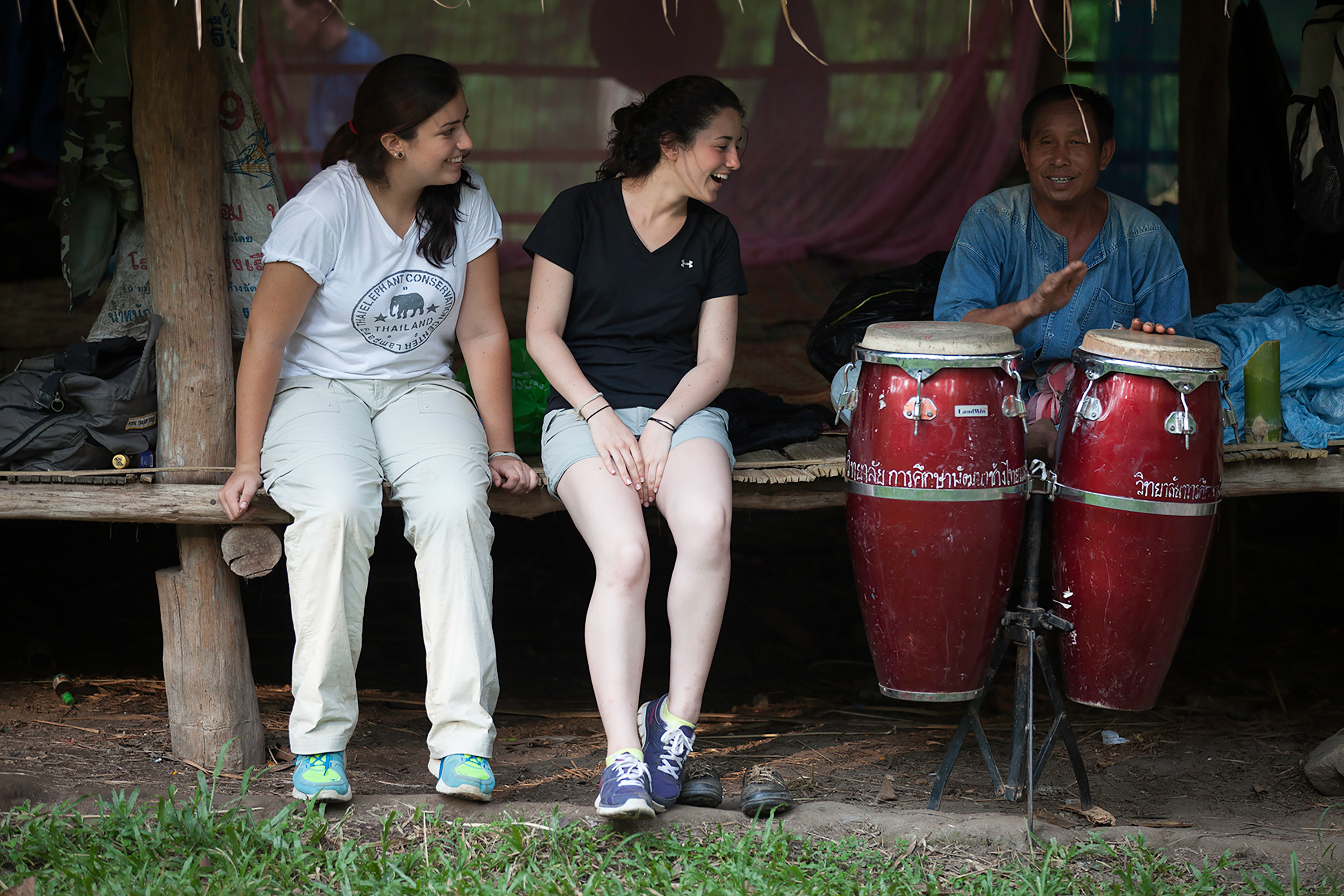 Two students listening to a man play the drums in Thailand.