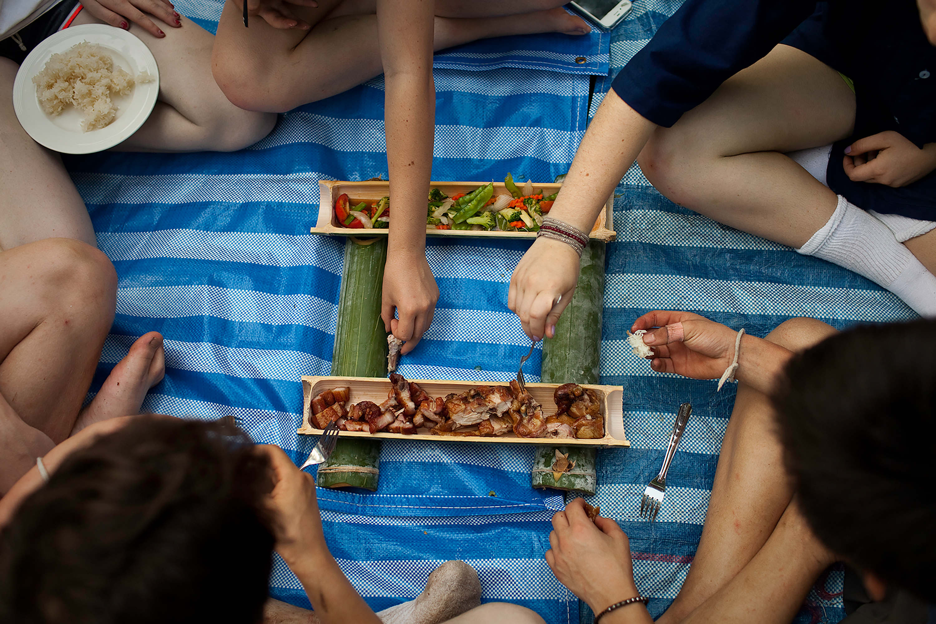 Students gathered around sitting on the floor sharing a meal in Thailand.