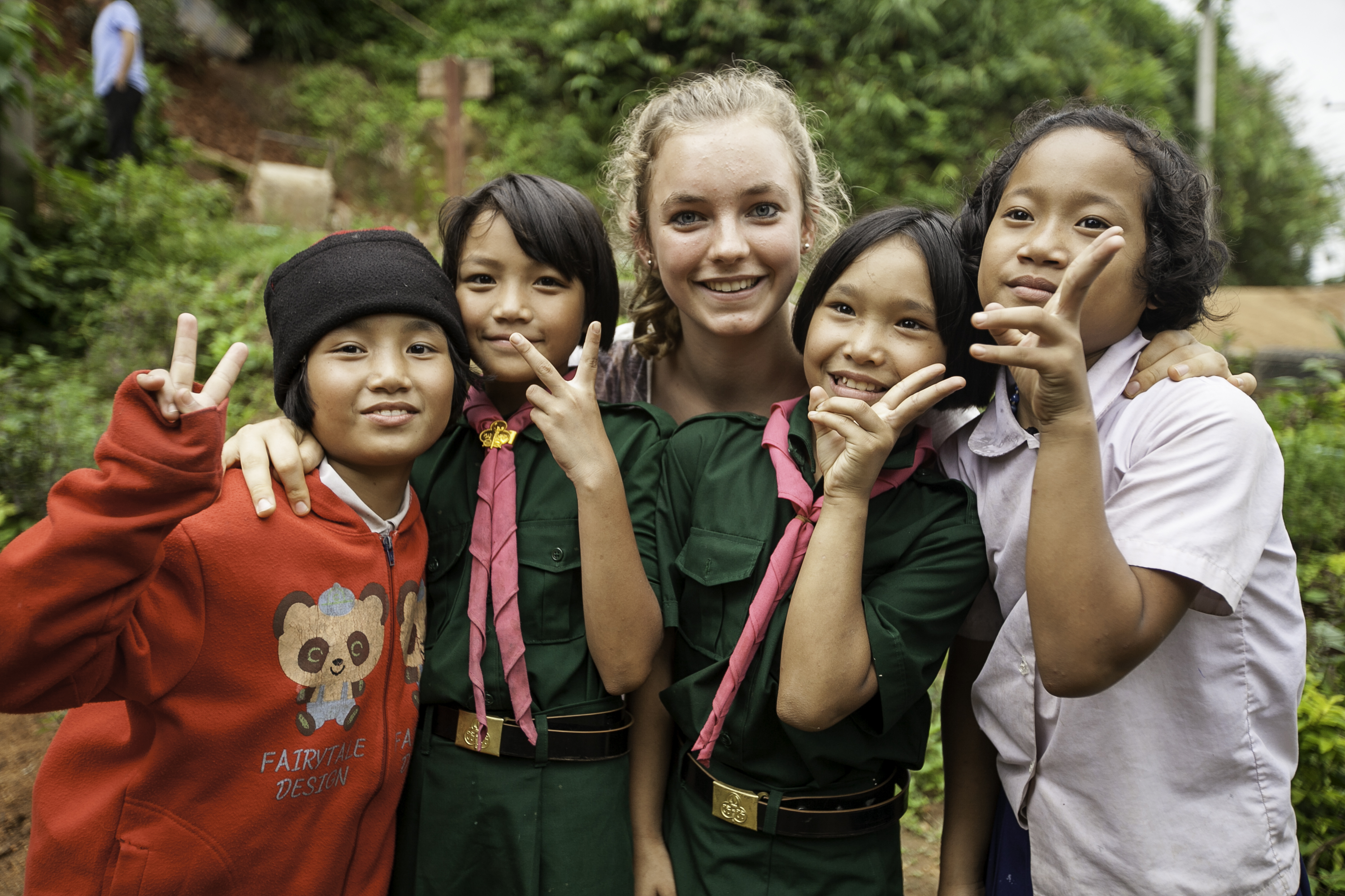 On a school trip, students flash peace signs with local schoolchildren in uniform outdoors