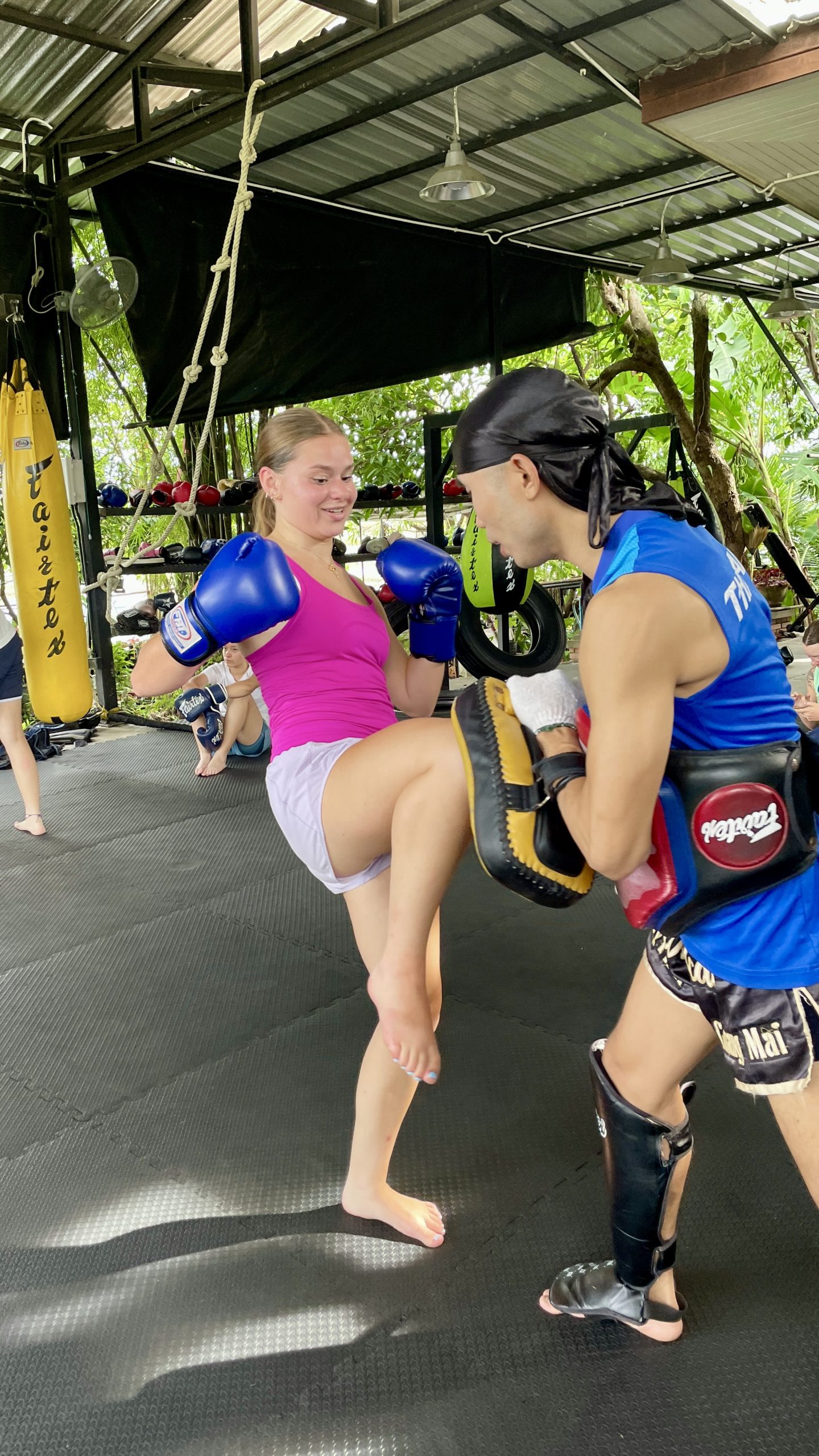 A student practices a knee strike on focus mitts during Muay Thai training