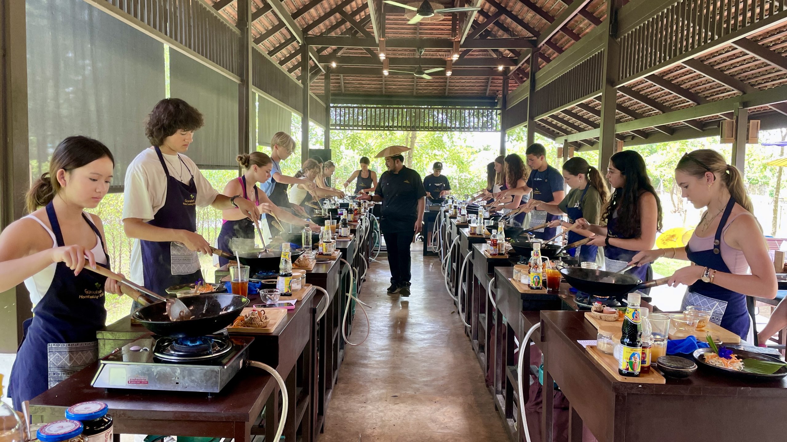 Students cook at individual wok stations in an open-air Thai cooking class pavilion