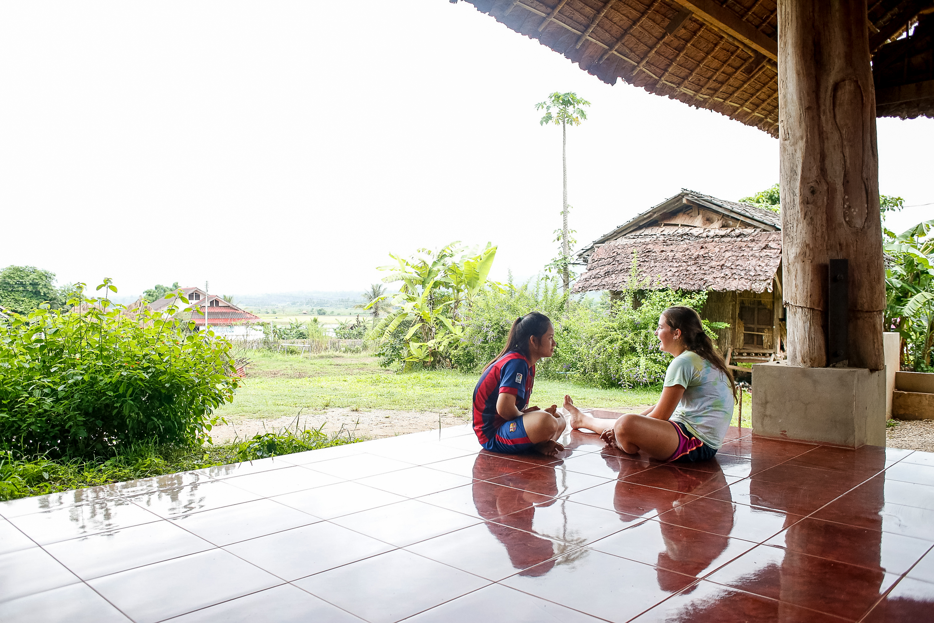 Students sit and chat on a covered tiled patio overlooking a rural landscape